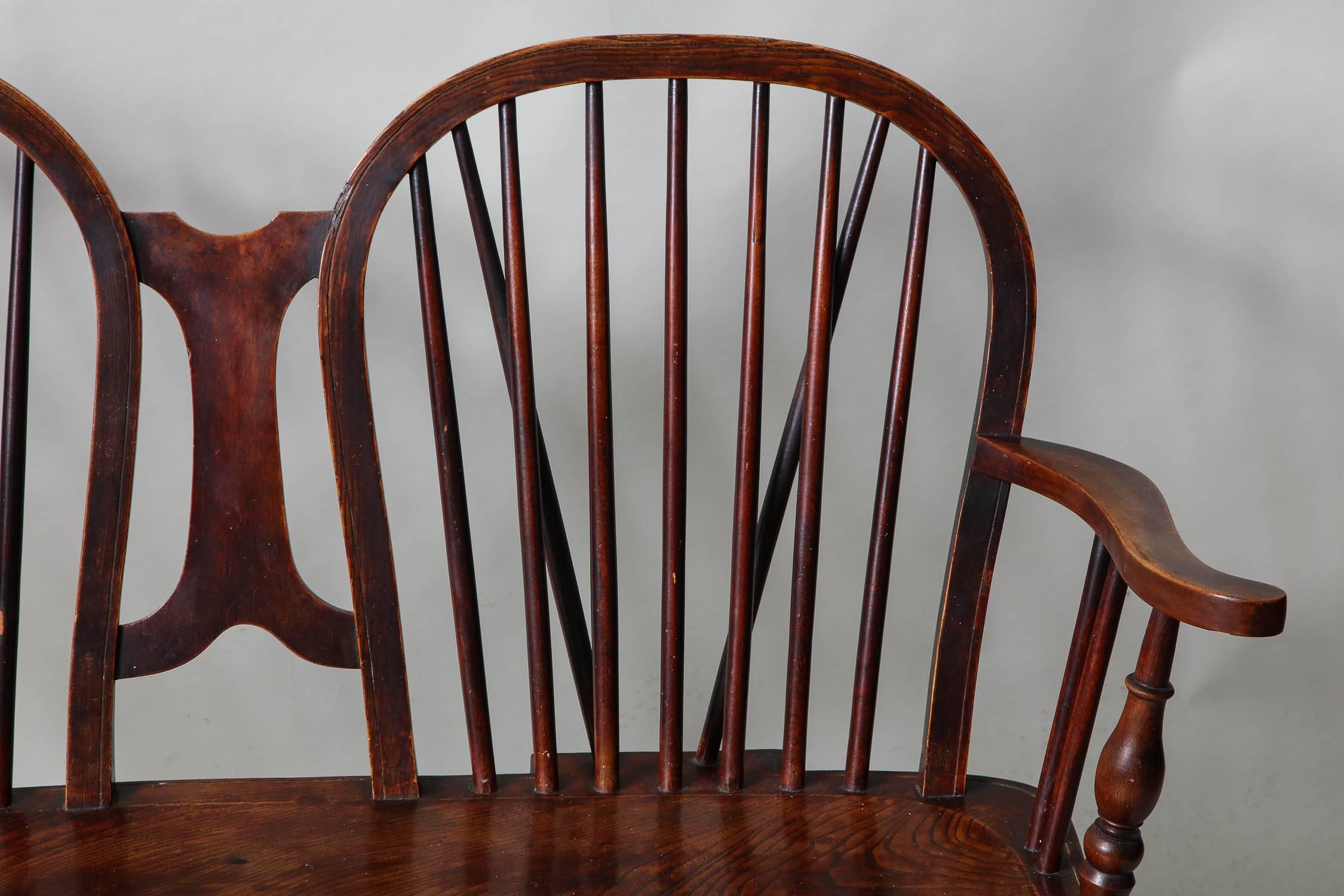 Unusual English double hoop chair back windsor settee in mixed woods, the two hoops with spindle supports and diagonal bracing, with turned arm supports over single plank elm saddled seat over turned legs joined by turned swell stretchers.