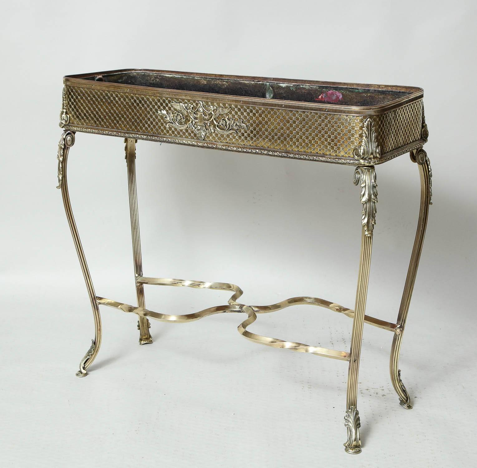 A French early 20th century brass conservatoire planter with reed-stitched decorated sides on shaped cabriole legs with acanthus decoration and elaborate H-stretcher, having original brass pull-out liner.