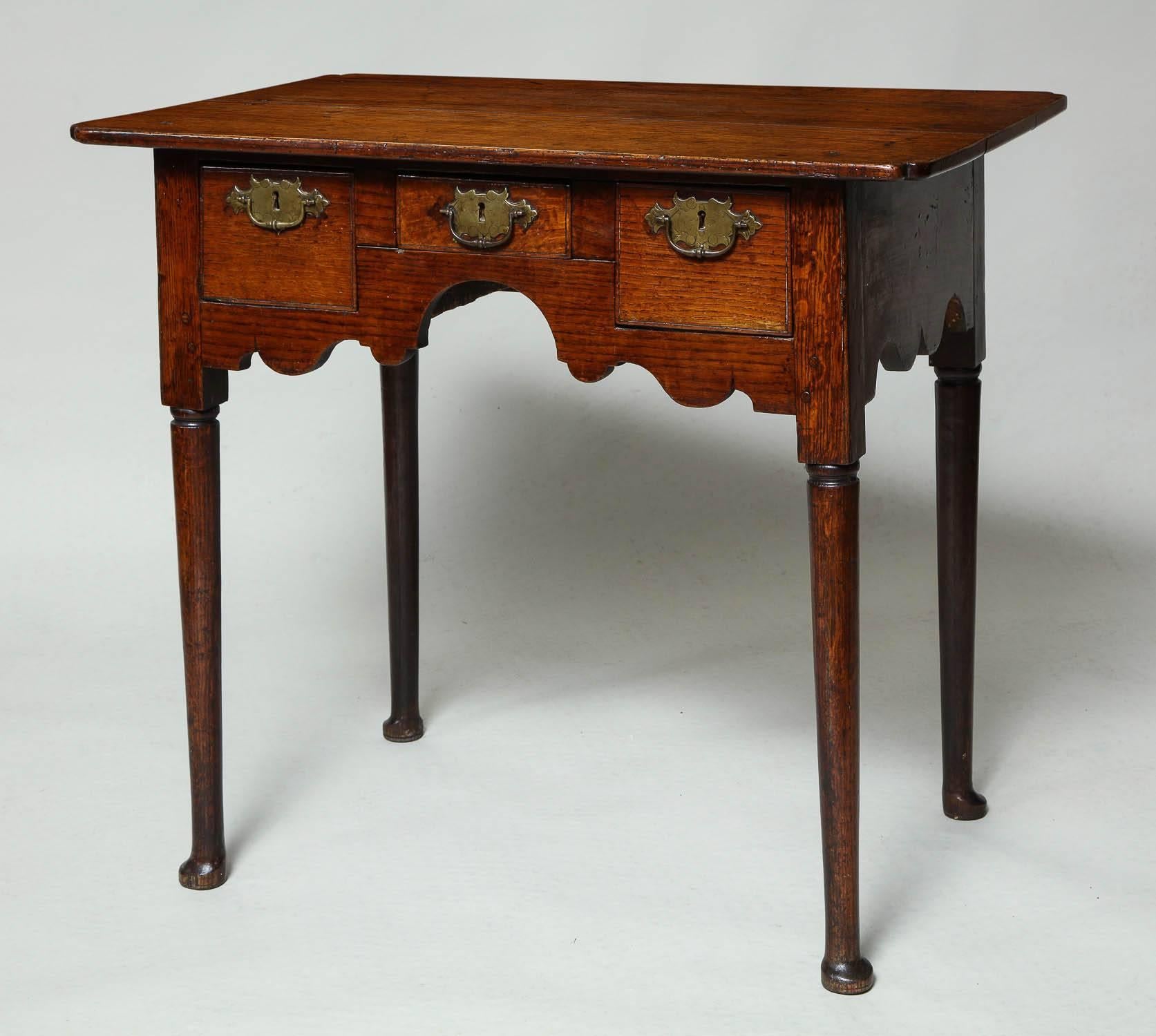 Very fine early 18th century English oak lowboy, the two plank top with re-entrant (baby's bum) corners, over two deep and one shallow drawer with original etched brass hardware, over richly scalloped apron and standing on ring turned legs ending in