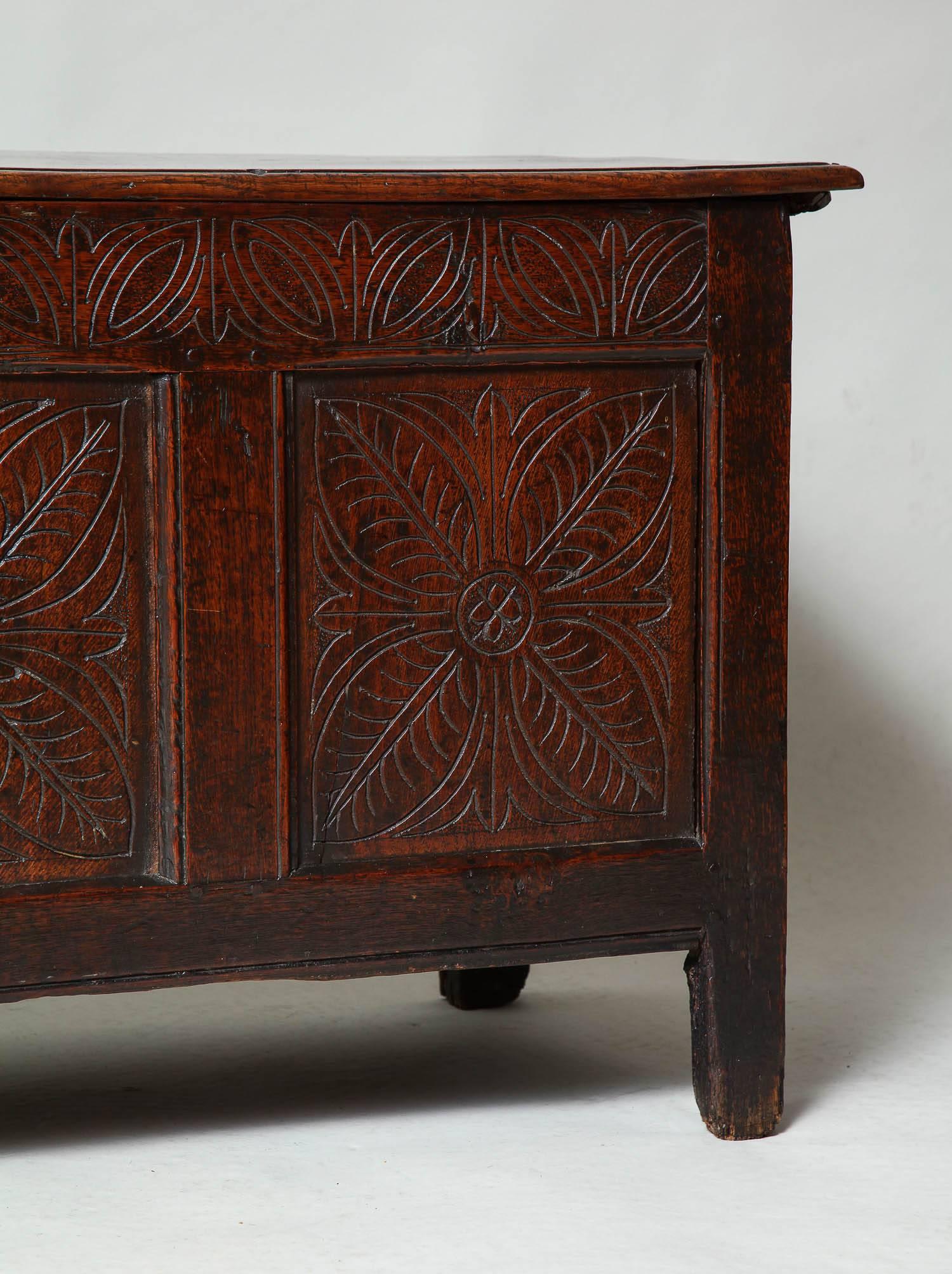 Fine Charles II period carved oak coffer having plank top and paneled carcass, the two board top with thumb molded edge, the three panels with quatrefoil shallow carving, the top rail with similarly carved lunettes and stylized tulips, two regional