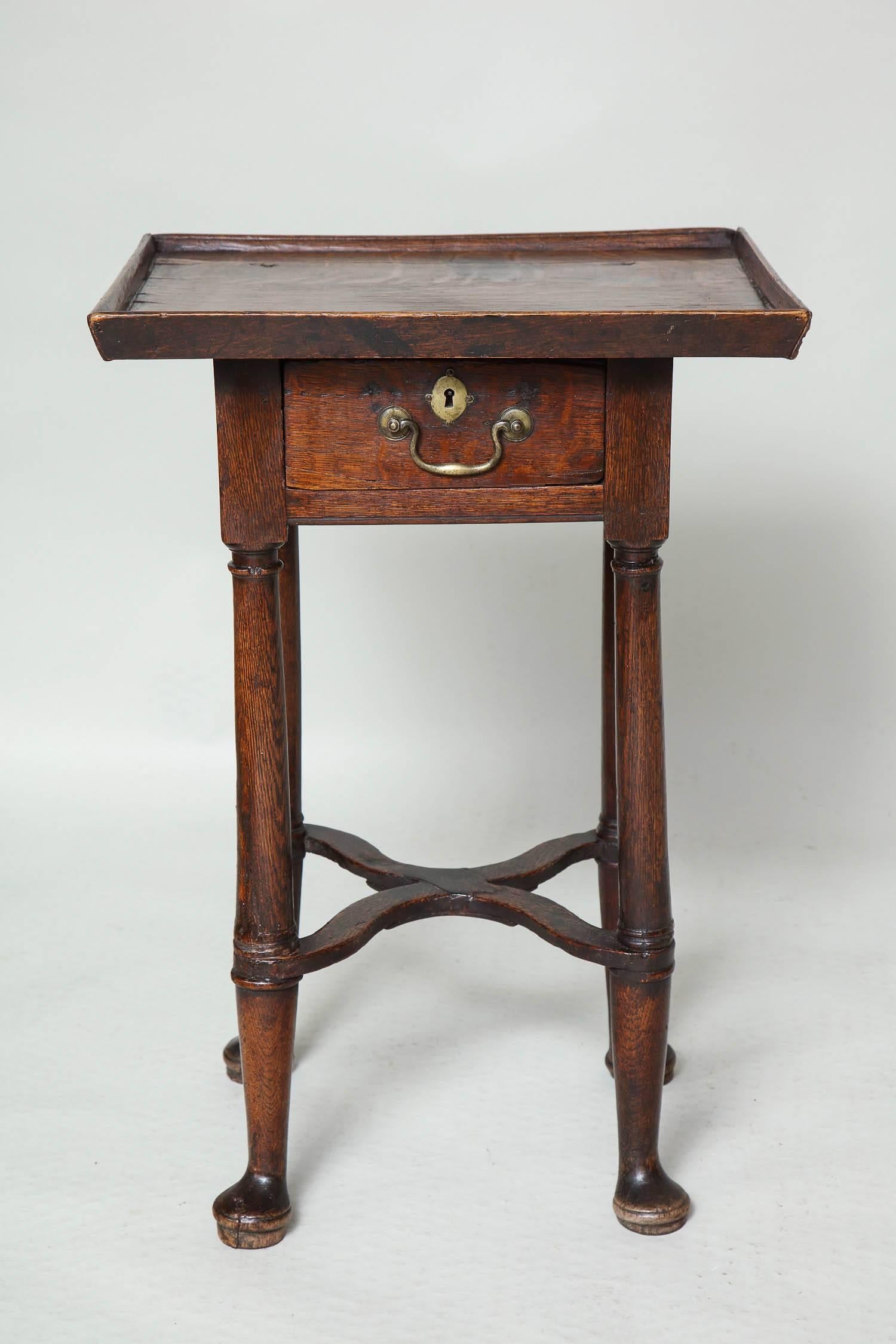 Charming and unusual English or Welsh oak side table with gallery edge over vividly grained top over single drawer retaining original hardware, over cannon barrel turned legs joined by archaic wavy X stretcher over turned pad feet.

This table