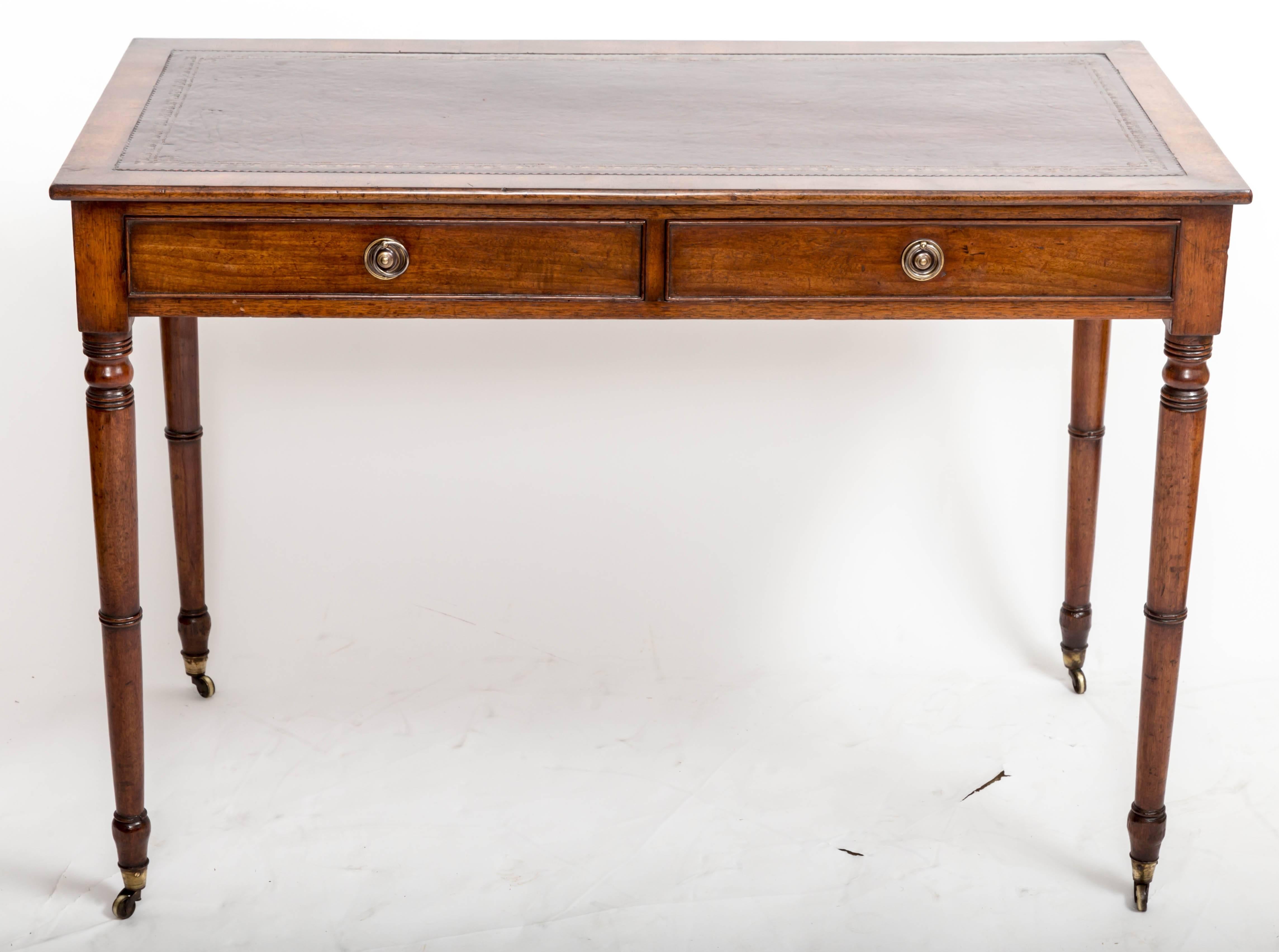 Two-drawer mahogany writing table with two drawers with brass pulls, turned legs with original brass casters and antique wine-colored leather insert. Measures: 42