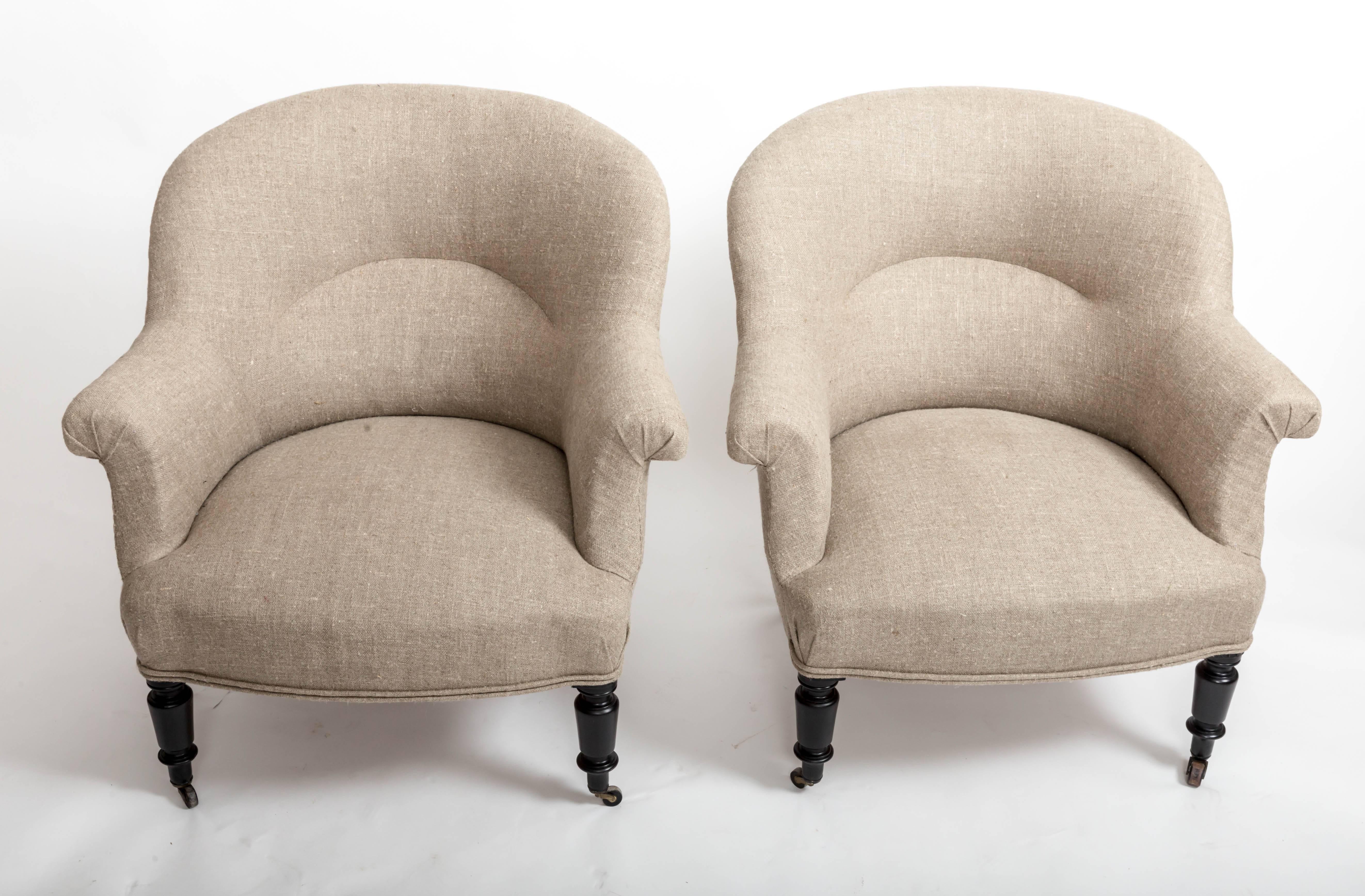 Pair of 19th century tub chairs with scrolled arms and newly upholstered in oatmeal colored French linen with double-welting sitting on ebonized turned front legs and splayed rear legs, both legs with casters.