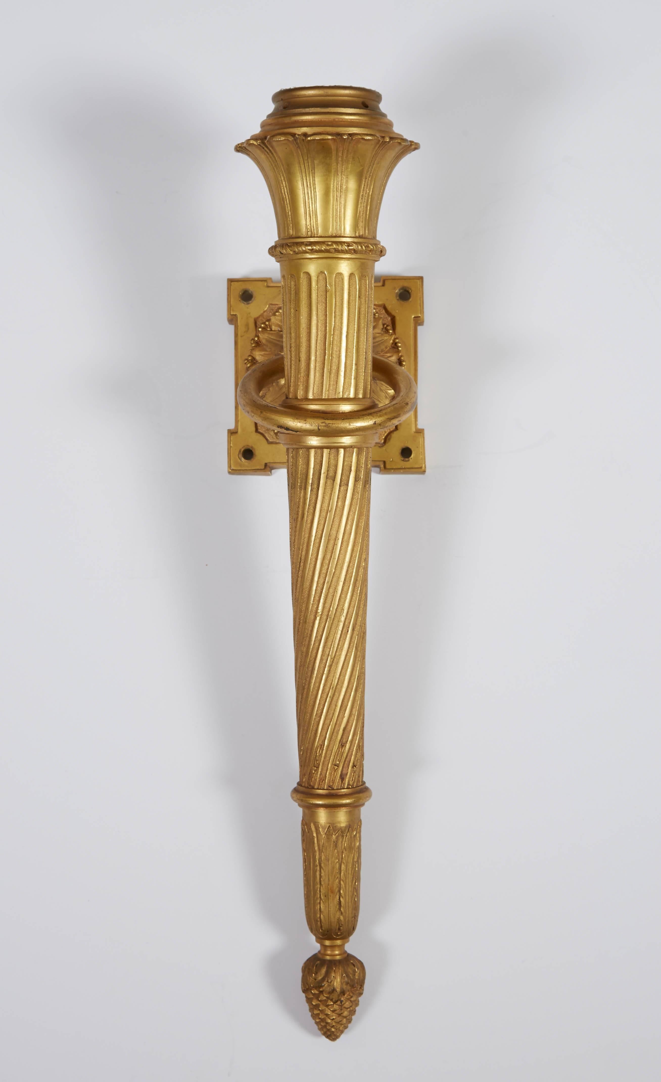A set of four ormolu neoclassical style torch form wall lights, spiral fluted torch held by lotus capped back-plate with ring suspension, the torch terminating in acorn finial.