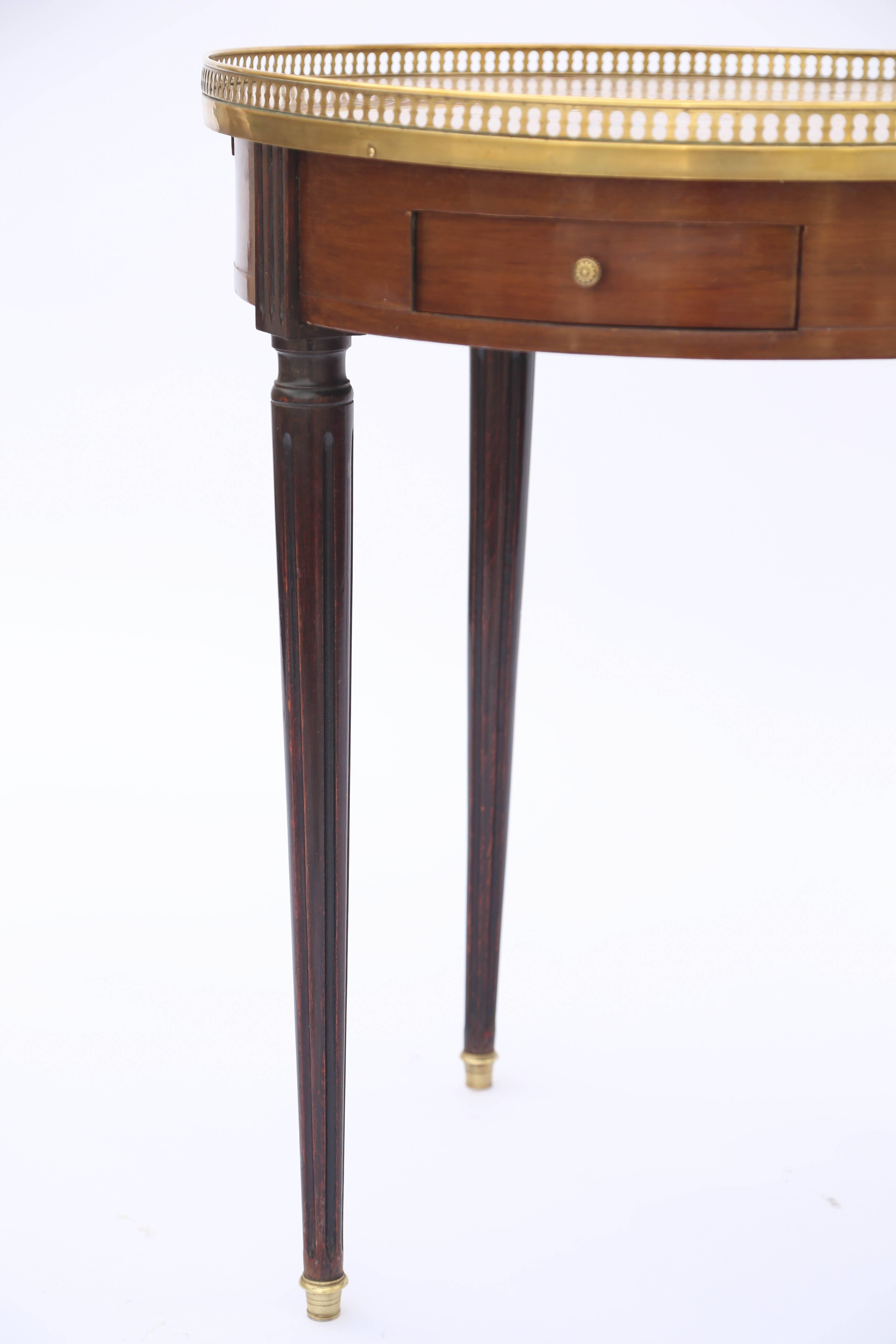 Bouillotte occasional table, having a round top of Breche D'alep marble, surrounded by a pierced gallery of brass, on mahogany table base, with double frieze drawers, and leather-clad slides, raised on round, tapering, fluted legs, ending in brass