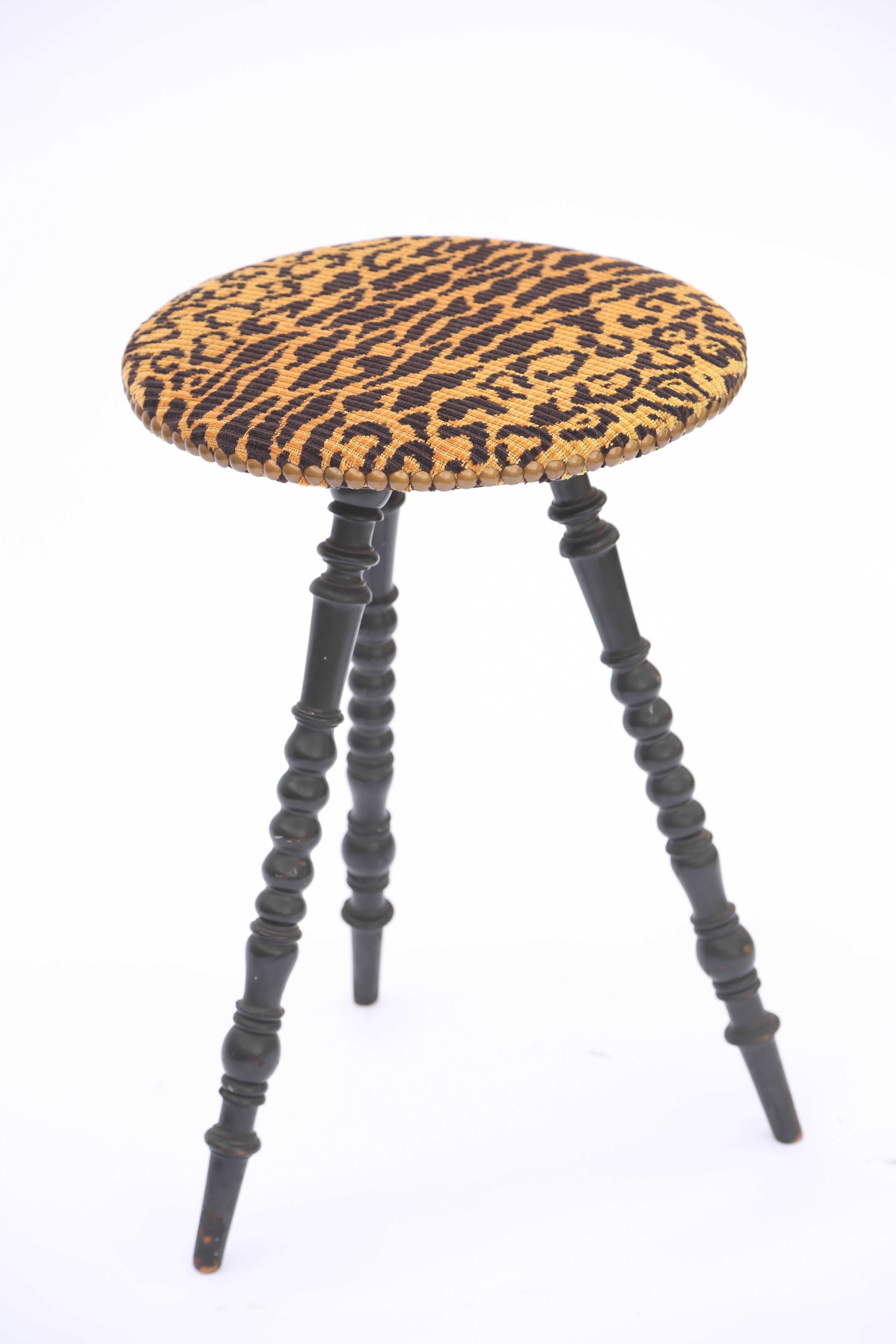 Occasional table having a round top upholstered in leopard fabric with nailheads, raised on a trio of turned legs in ebonized wood, ending in touipe feet. 

Stock ID: D4646.