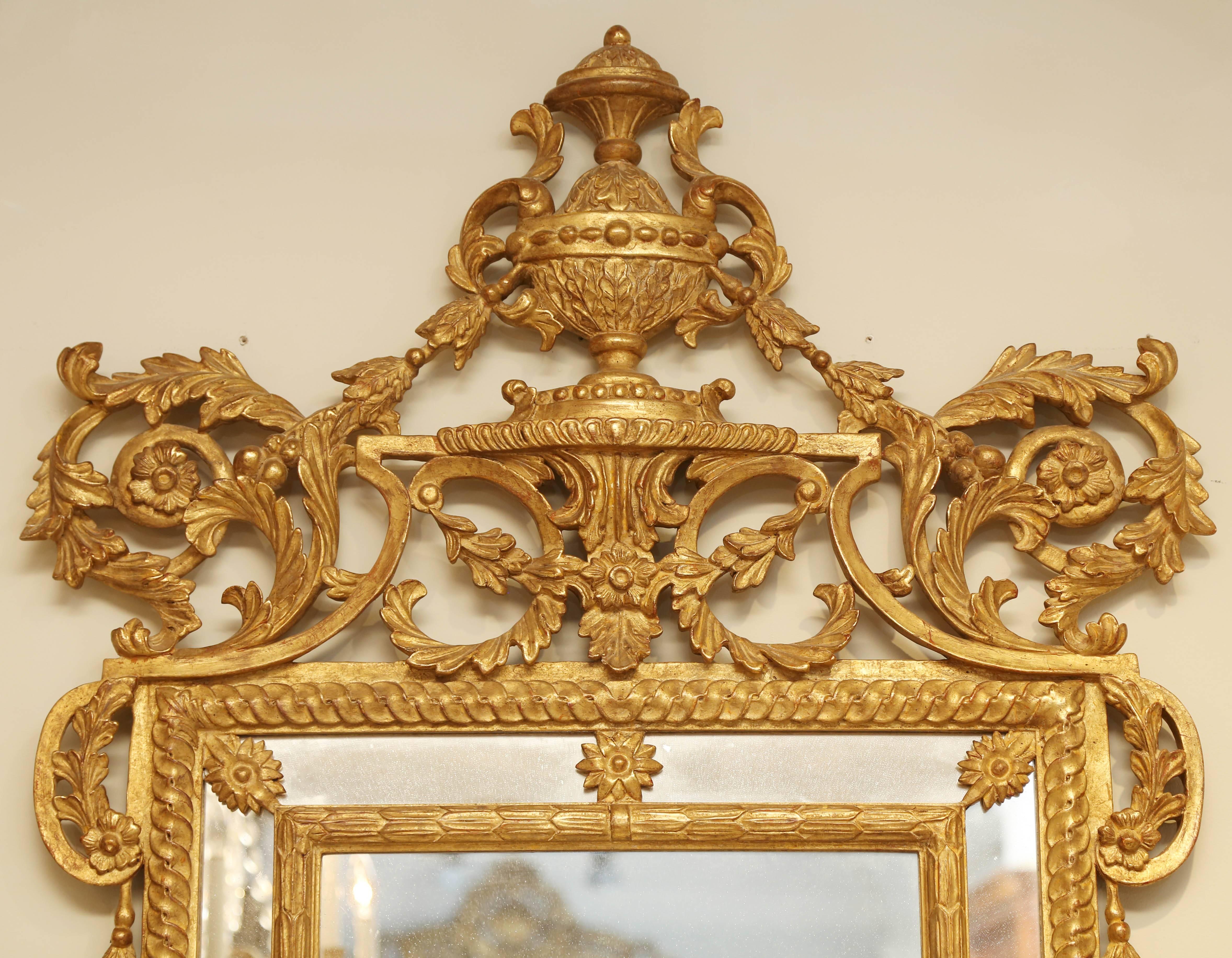 Pair of mirrors, in Louis XVI taste, of hand-carved giltwood, having an elaborate pierced scrolling pediment, centred with an urn, its rectangular frame with mirrored relief, decorated by rosettes, and draped with husking.

Stock ID: D4895