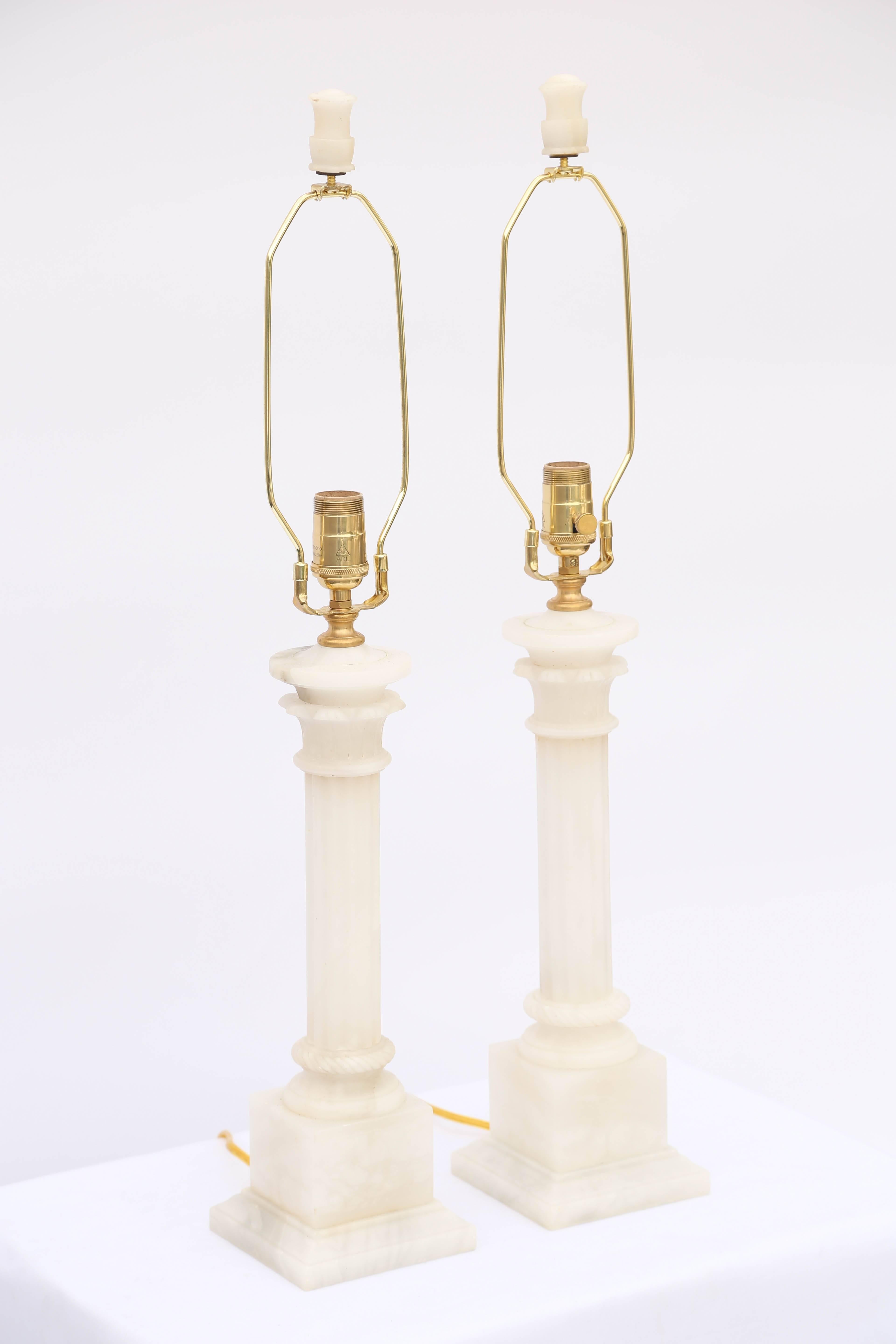 Pair of table lamps, of carved alabaster, each a round, fluted column with stylized capital, its round foot base on graduating square plinth. With matching finial.

Measured to top of socket. 

Stock ID: D6546.