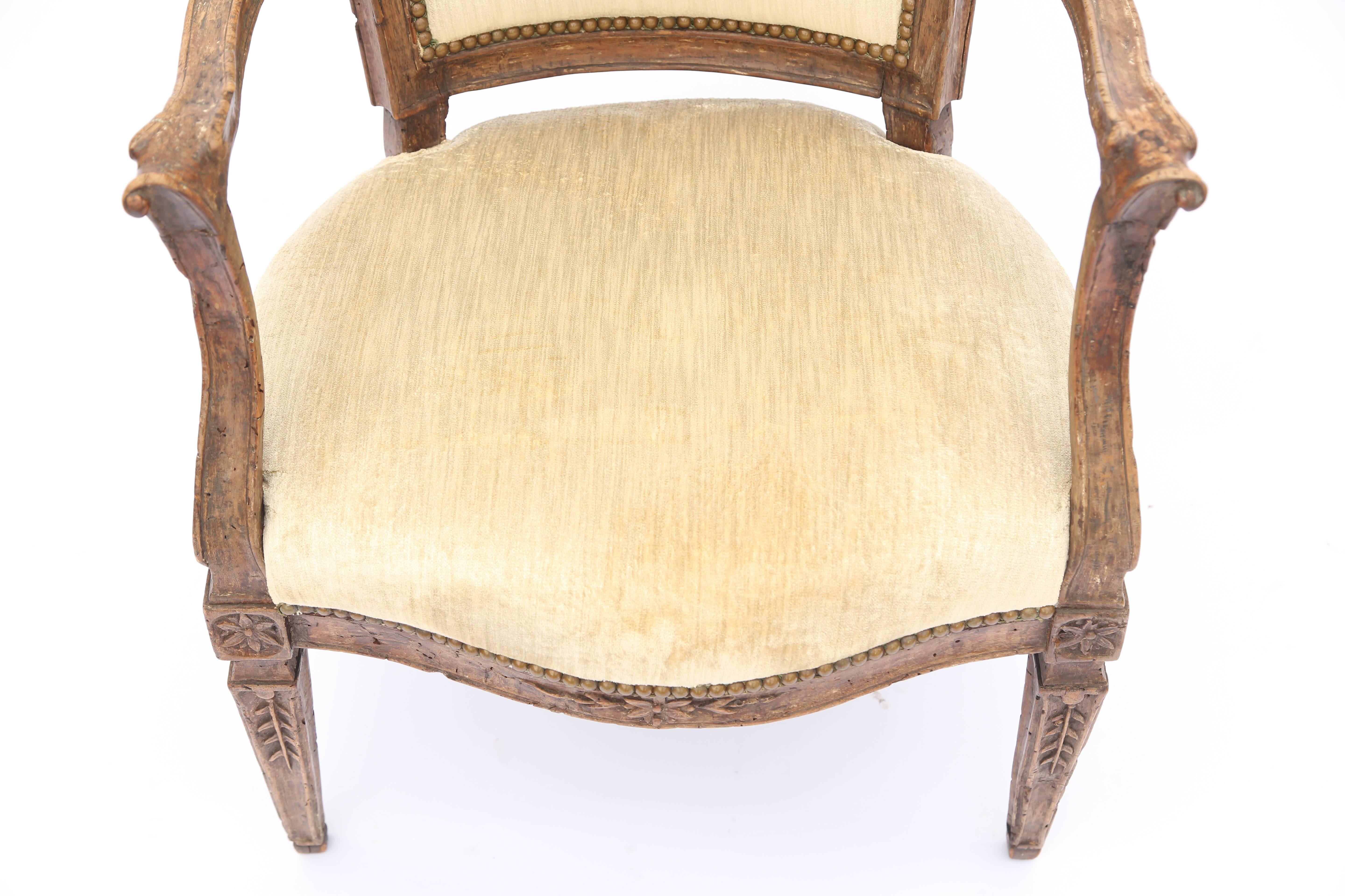 Pair of fauteuils, of walnut, each having a padded, square, molded back accented by a small floral carving, the outward-curved arms, ending in scrolls, and raised on down swept terminals, flanking its crown seat, the bowed seat rail carved with