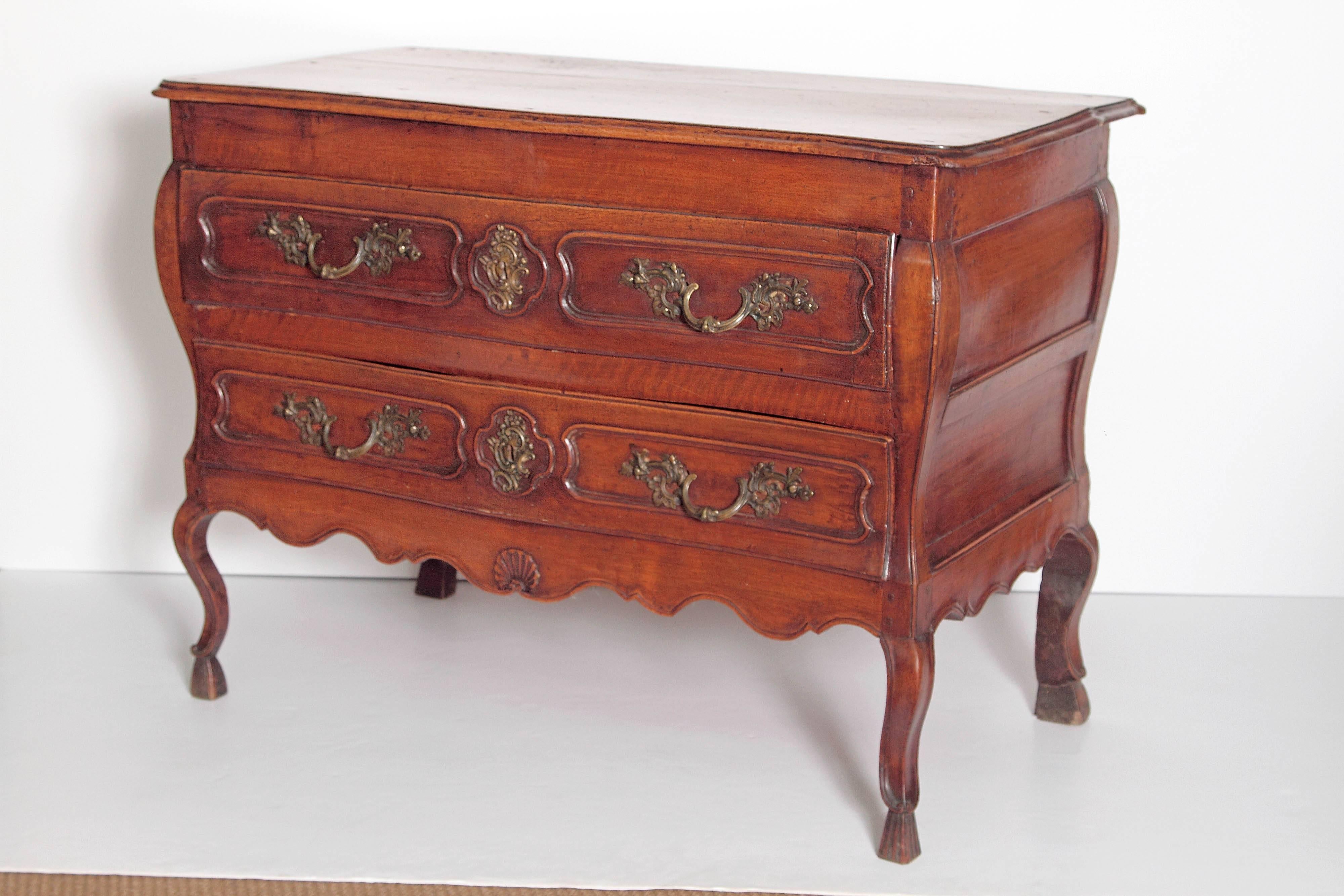 A Louis XV period two-drawer chest of walnut. Panels on drawers and casual curving apron. Stands on cabriole legs with hoof feet. Ornate drawer pulls and escutcheons.