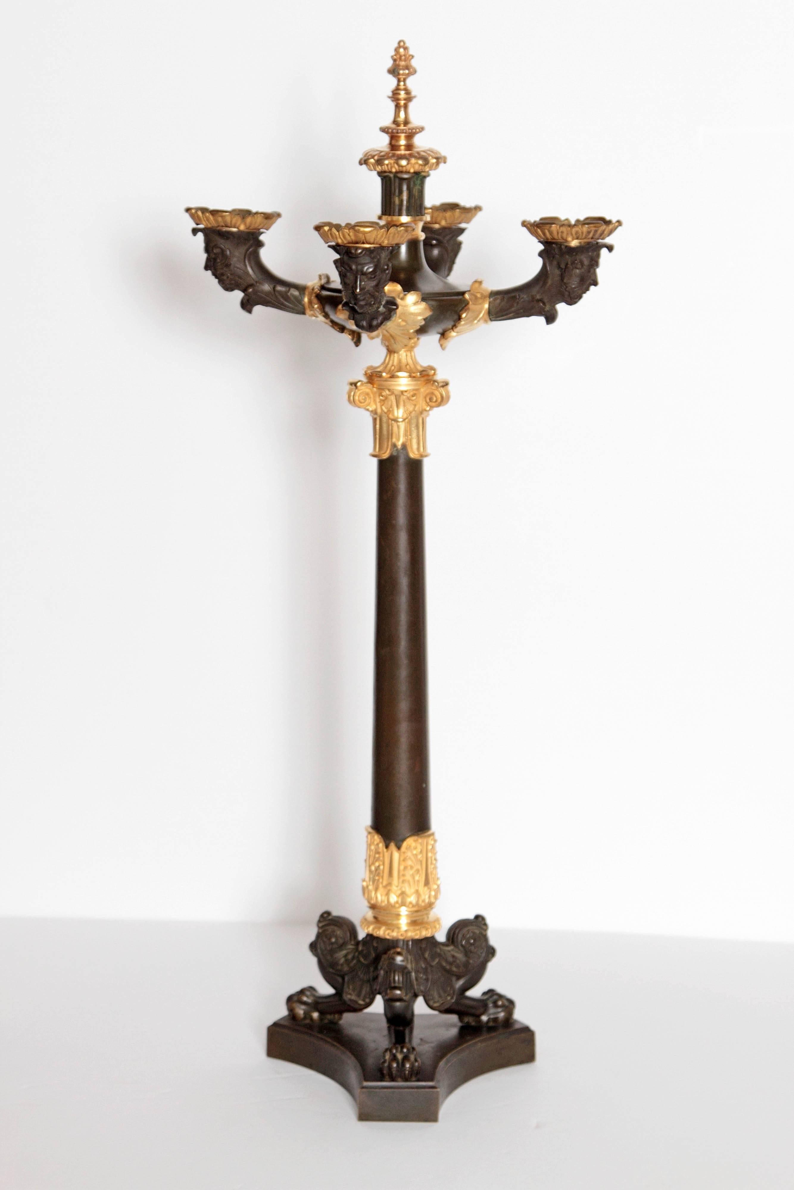 A pair of Charles X patinated and gilt bronze four arm candelabra. Four candle arms have heads below holders. Columns are formed on triangular bases with lion's heads and paw feet, French, 19th century.