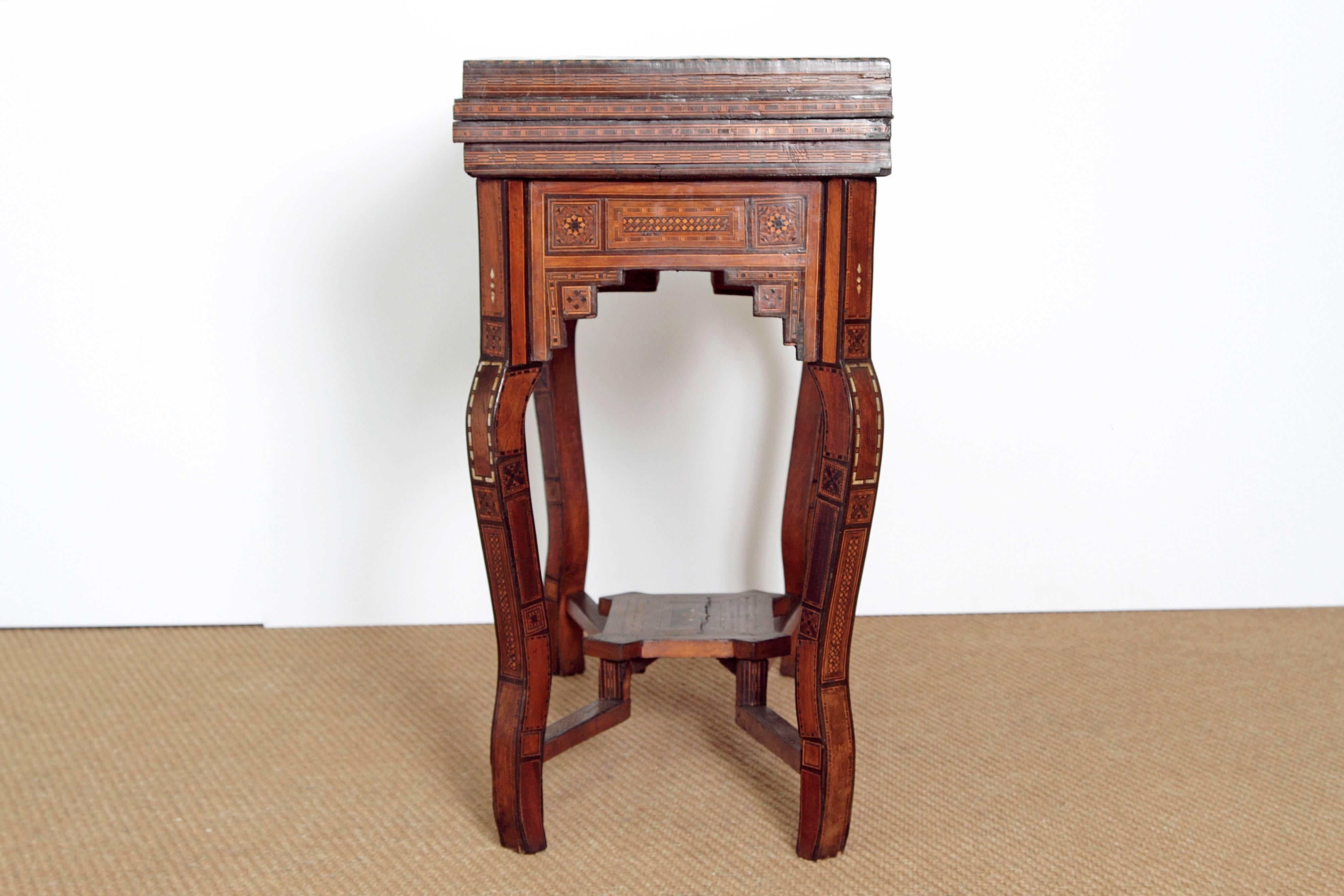 A beautifully shaped Syrian games table inlaid with ebony, various species of exotic woods and mother-of-pearl in geometric patterns. Rectangular top opens up into a square top with a green velvet surface. The velvet top is hinged and opens to