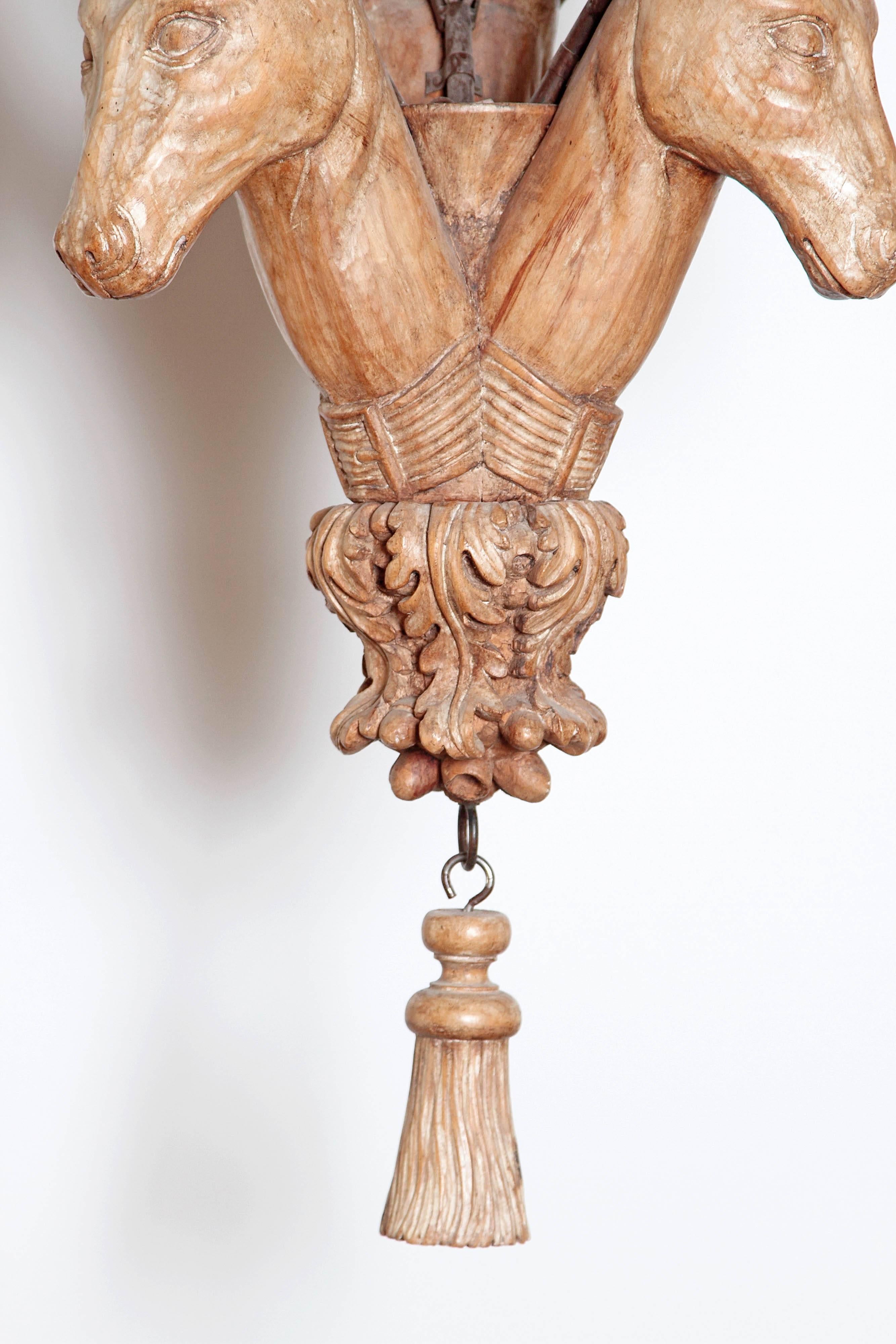 A large carved wooden chandelier with three deer heads with antlers holding the candle lights. A natural style in bleached wood with leaves at base, England, 20th century.