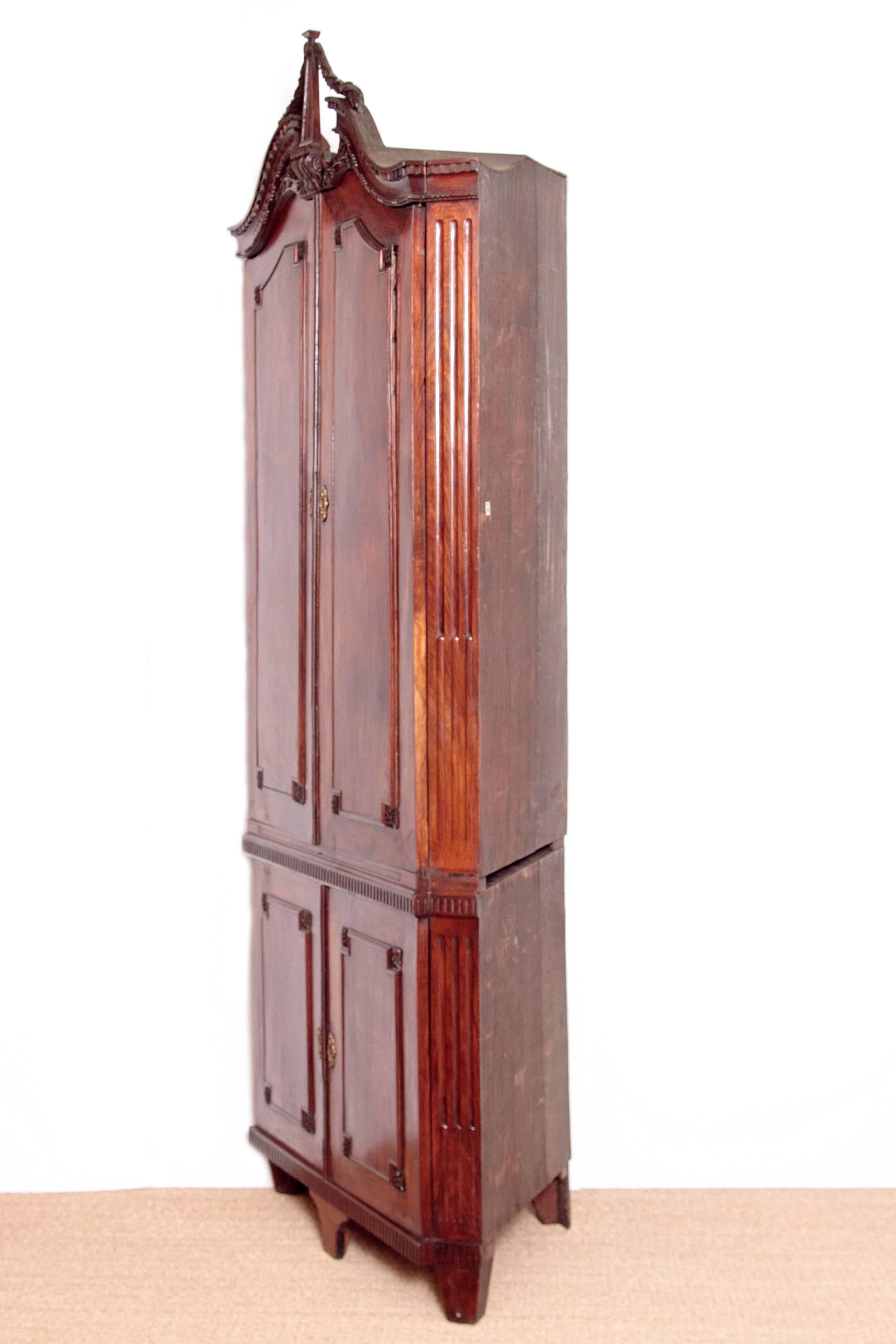 An 18th century continental corner cabinet of mahogany in the English taste with split pediment at top with dentil detailing. Carved swag attaches the centre column. Carved floral detail below. Upper two doors with interior shaped shelves and two
