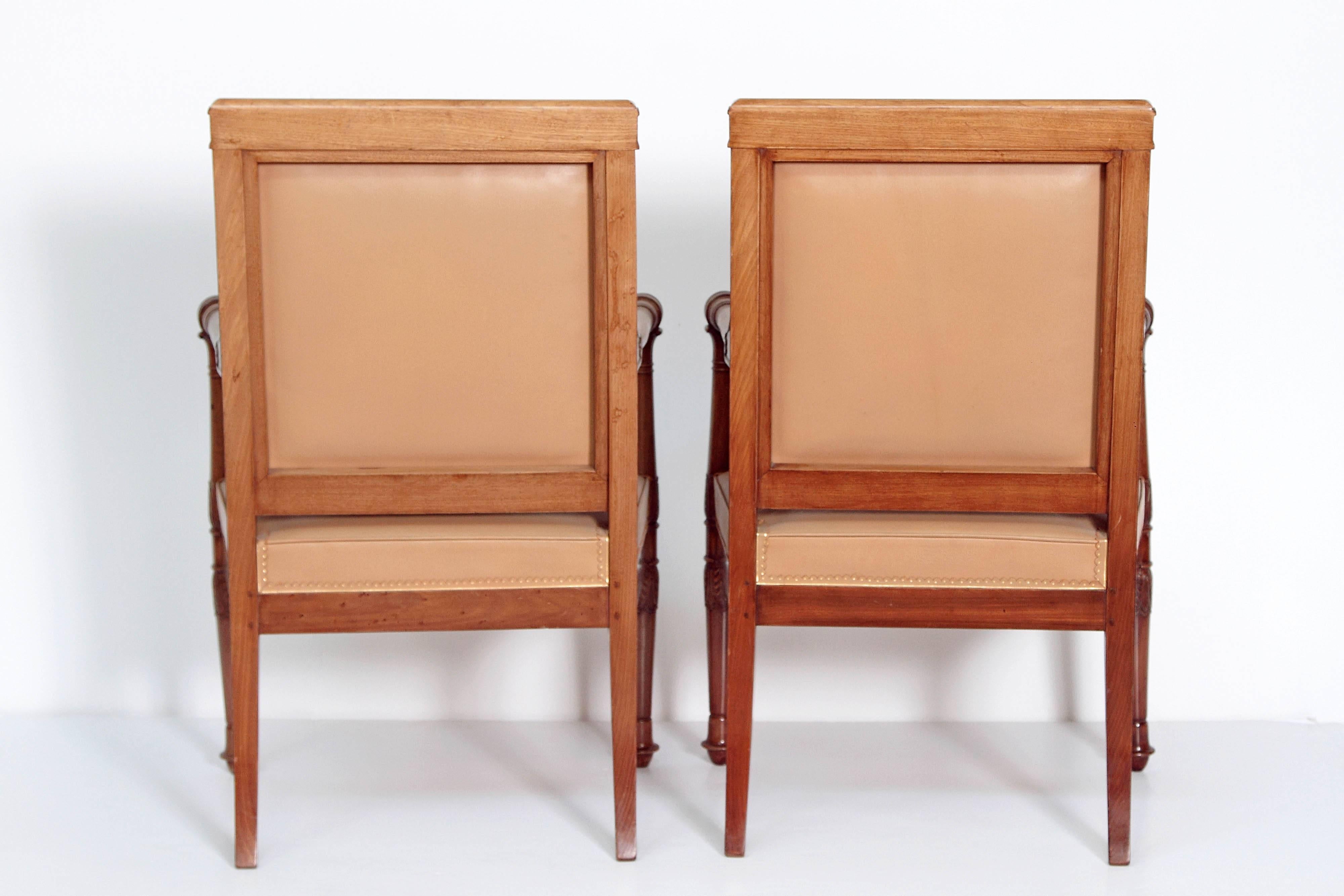 Pair of Empire armchairs, mahogany with turned arms and tapered legs, rectangular back, upholstered in rich tan leather with gilt leather trim, Christie's label.
  