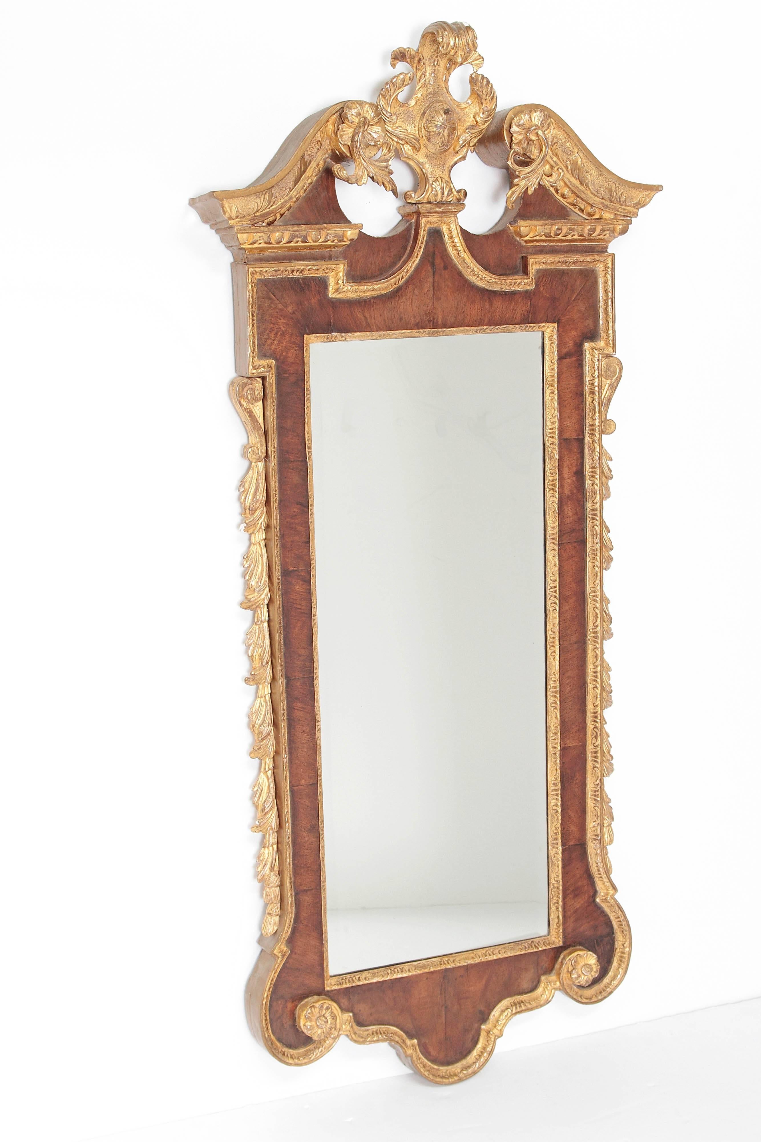 A George II mahogany pier mirror with elaborate gilt trim. Topped with a broken pediment with wreath and plum in center. The mirror is beveled, mid-18th century, England.