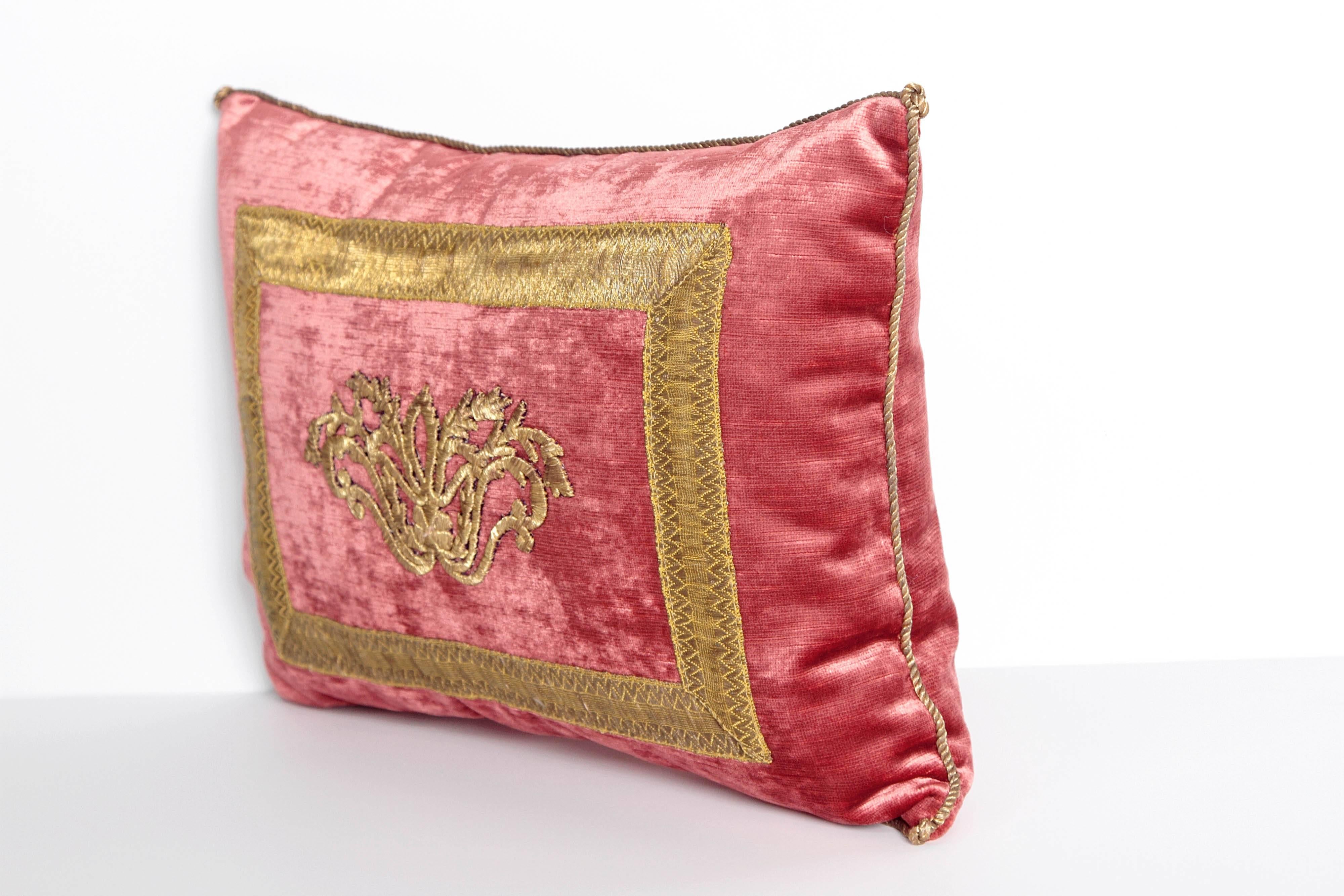 A pillow of antique Ottoman Empire raised gold metallic embroidery framed with antique gold metallic galloon on faded red velvet fabric, hand trimmed with vintage gold metallic cording knotted in the corners, down filled.