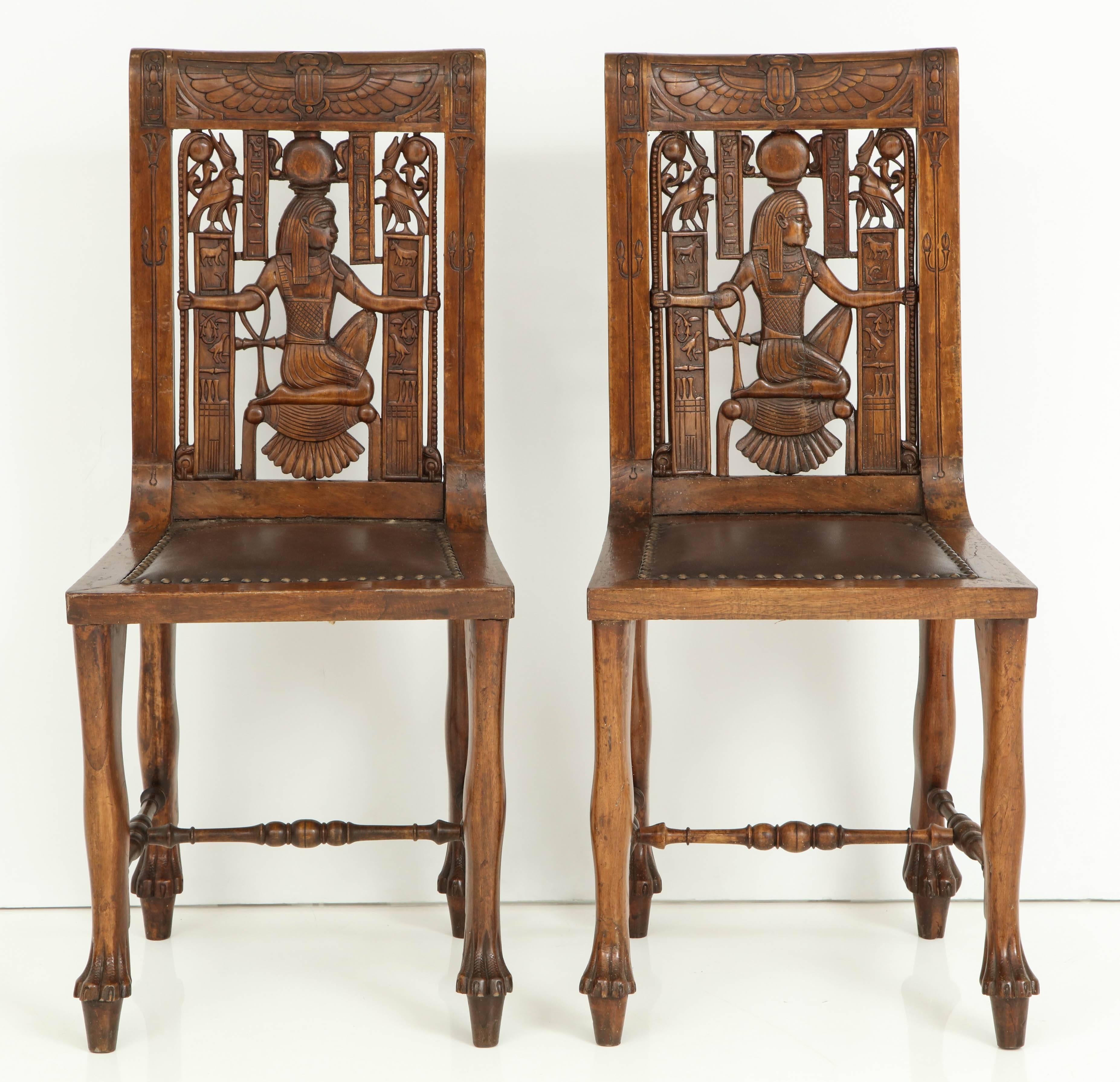 A pair of Continental carved fruitwood Egyptian Revival sidecars, circa 1900, with elaborately carved ancient Egyptian style carvings throughout and leather upholstered seats. 

A fantastic pair of accent conversational chairs.