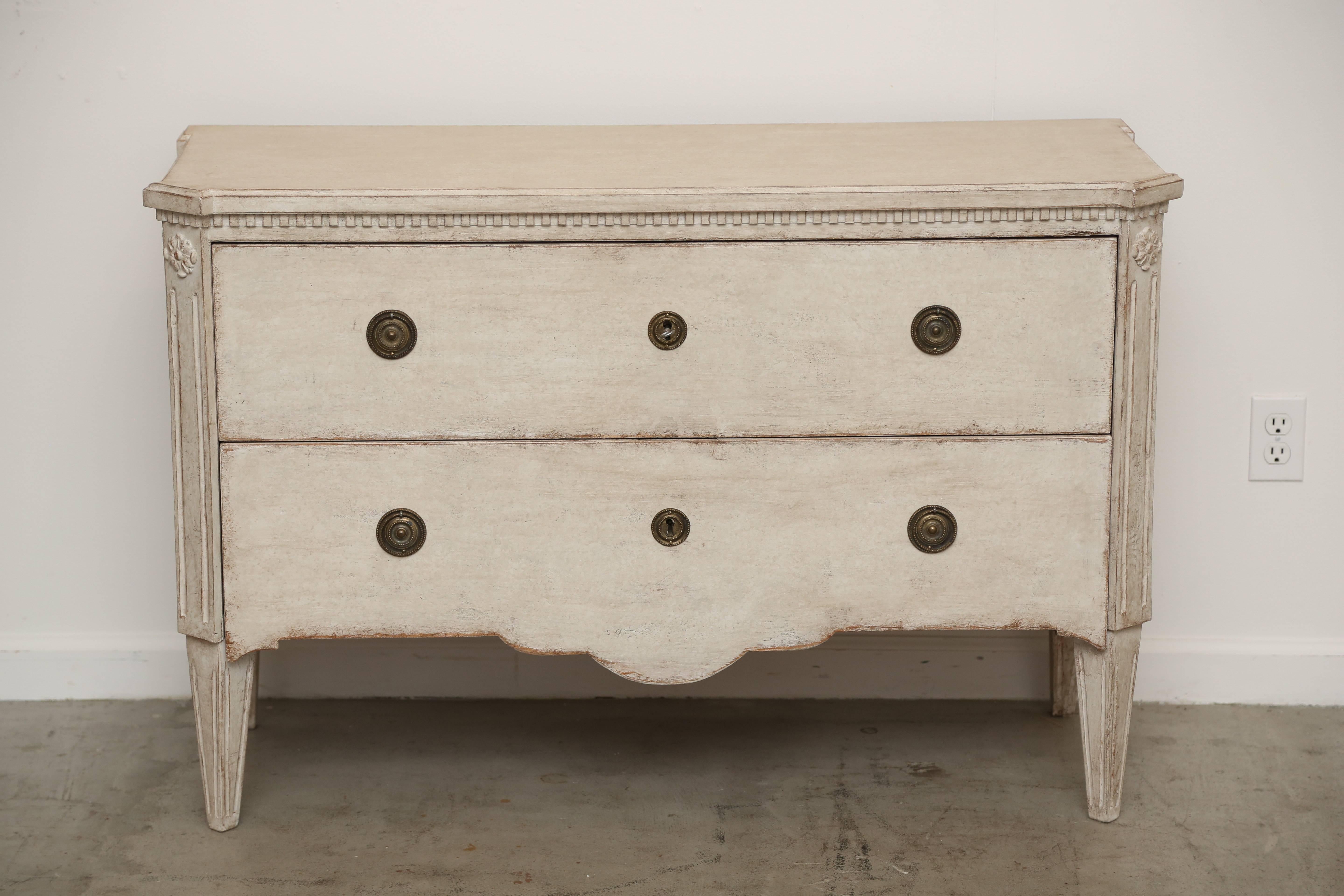 Antique Swedish Gustavian white distressed painted two-drawer chest.
The top is shaped at the corners with a small convex edge, below the top is a
small dental molding border. There are cut corners with a craved rosette and 
fluted panel, classic