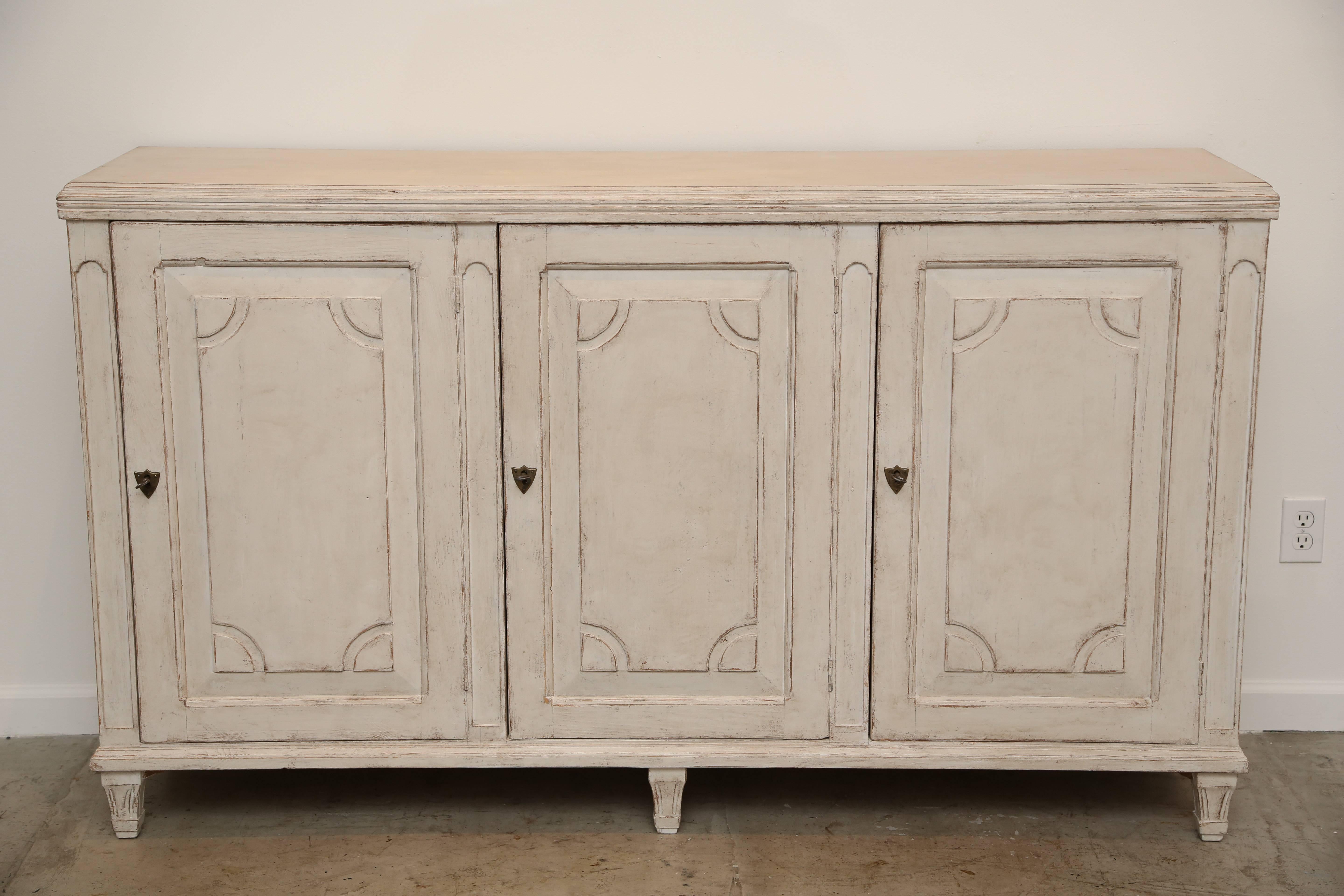 Antique Swedish Gustavian style three door sideboard, with raised panel doors,
the corners of the panels have cresent shape cut-out, carved border around top of cabinet, arched carved panels between the doors. One interior shelf and
bottom shelf.