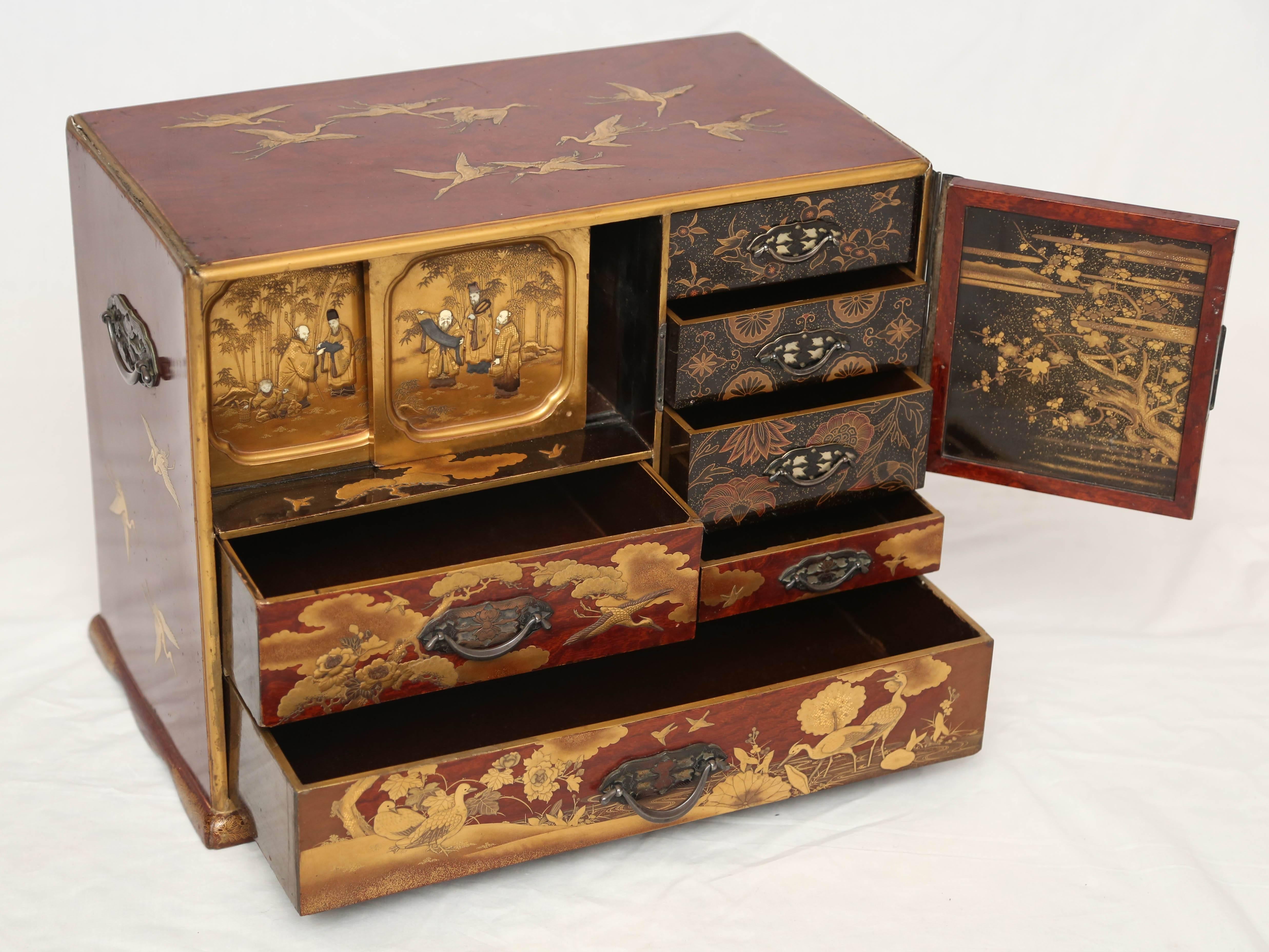 A Japanese parcel-gilt brass and bone decorated veneered Keyaki elm Meiji Period (1868-1912), and late 19th century, the rectangular top decorated with nine cranes in flight over a cupboard door at right with a decorative floral zagane and