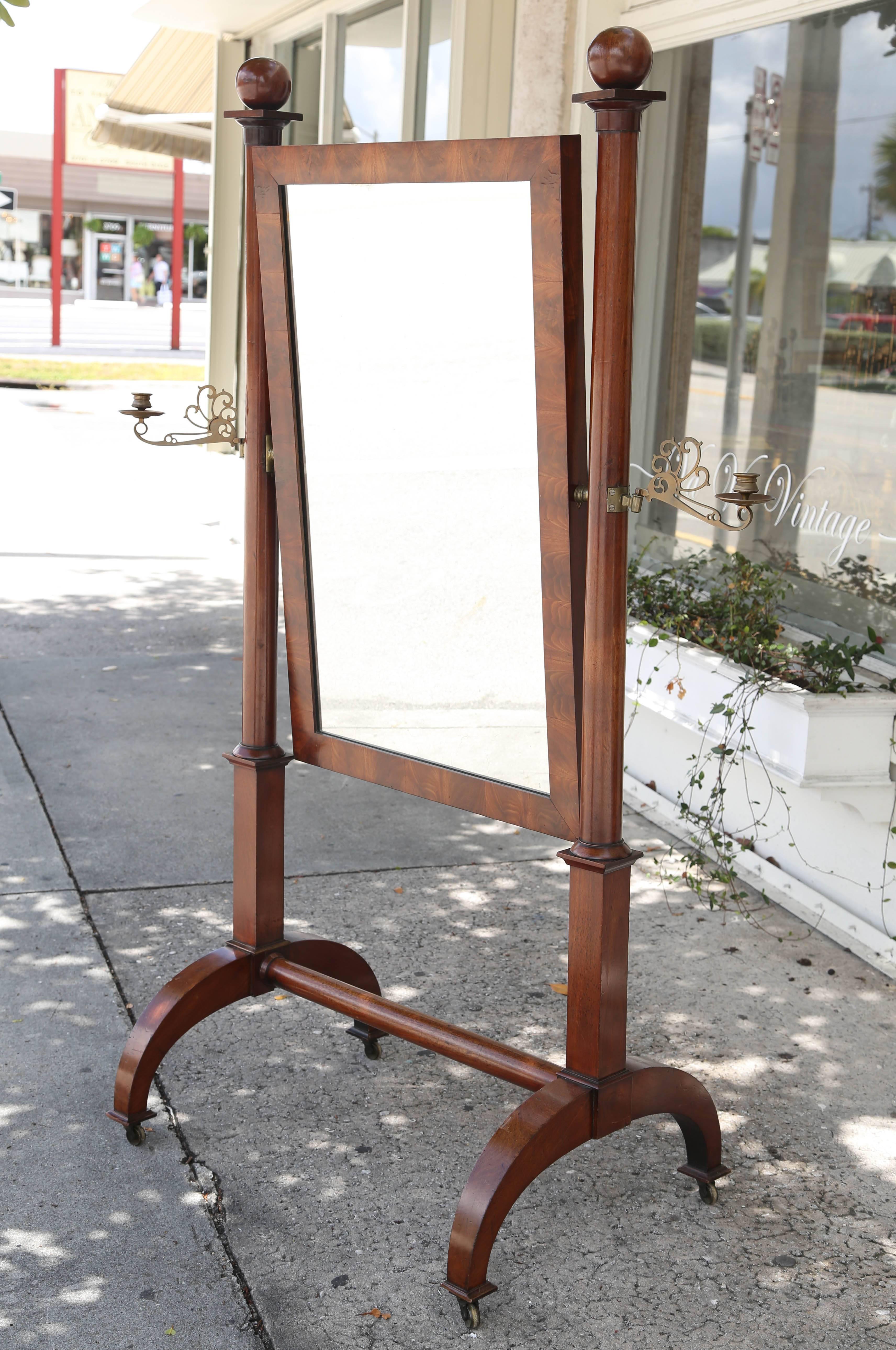 This is a superb quality cheval mirror with globular finials and columnar supports uniting a rectangular hinged frame and fitted with candle arms on a trestle base, raised on casters.