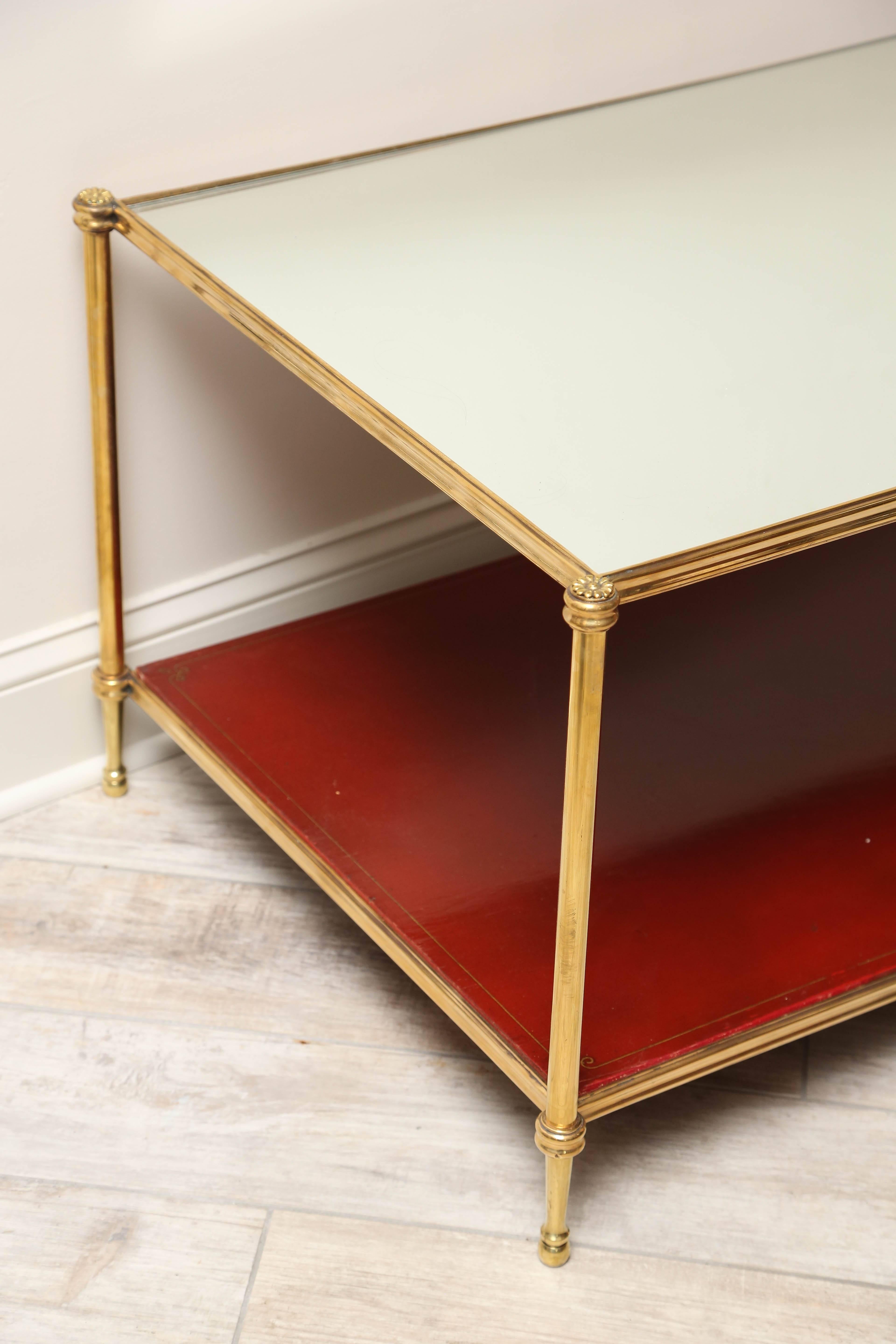 Two-tiered brass coffee table with mirrored top and red lacquered bottom shelf.