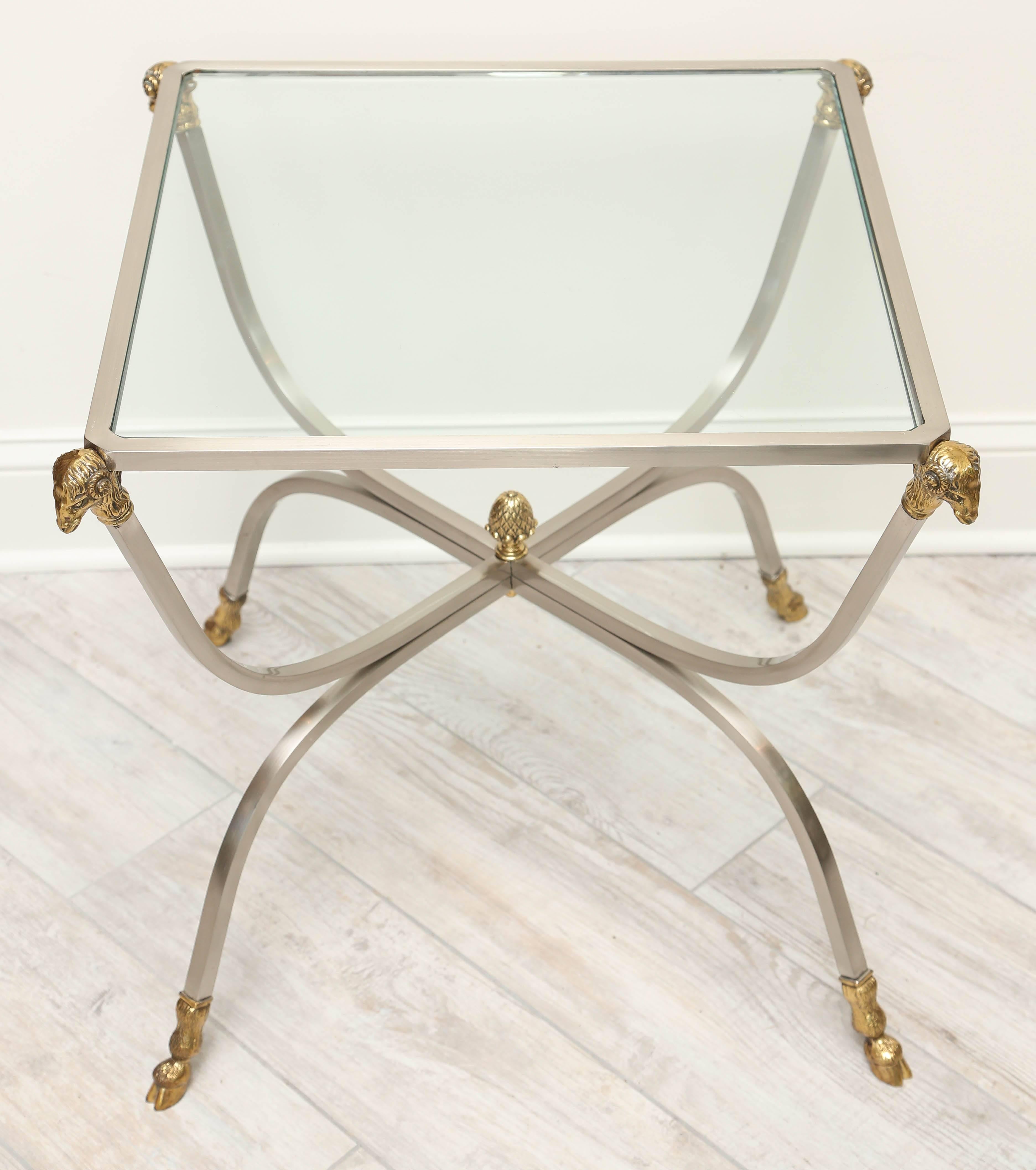 Classical pair of steel and brass glass topped side tables with ram's heads in each corner and hoofed feet.