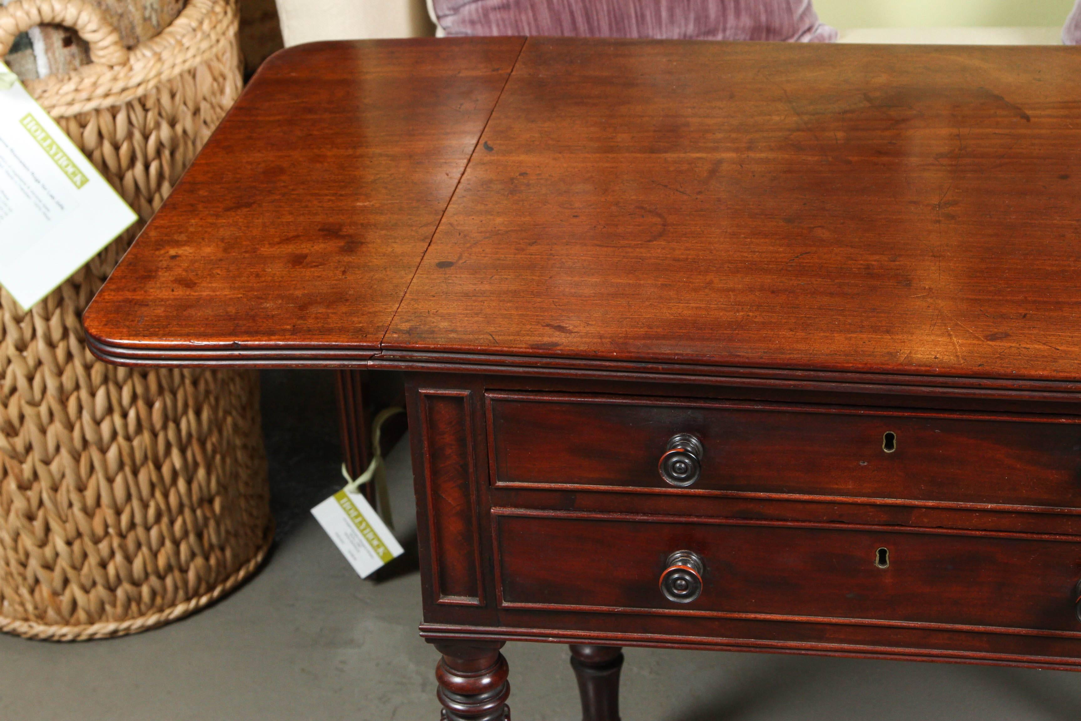 A fine English mahogany drop-leaf pembroke work table in the manner of Sheraton, featuring a rectangular top with fold-down sides. Two drawers with brass casters.