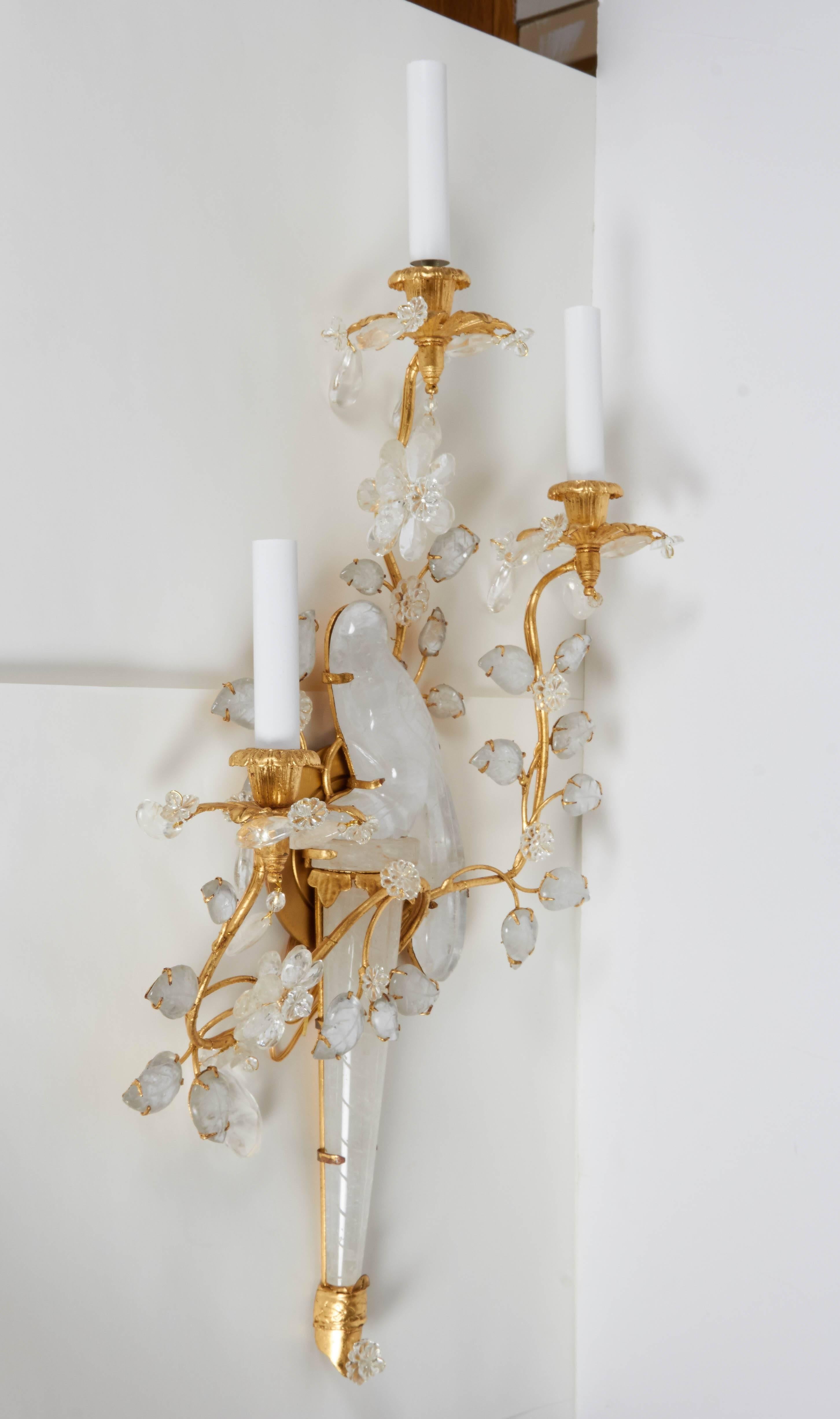 A pair of symmetrical right and left facing three-light gilt metal sconces, design of bird and rock crystal surrounded by sprays of branches and leaves.