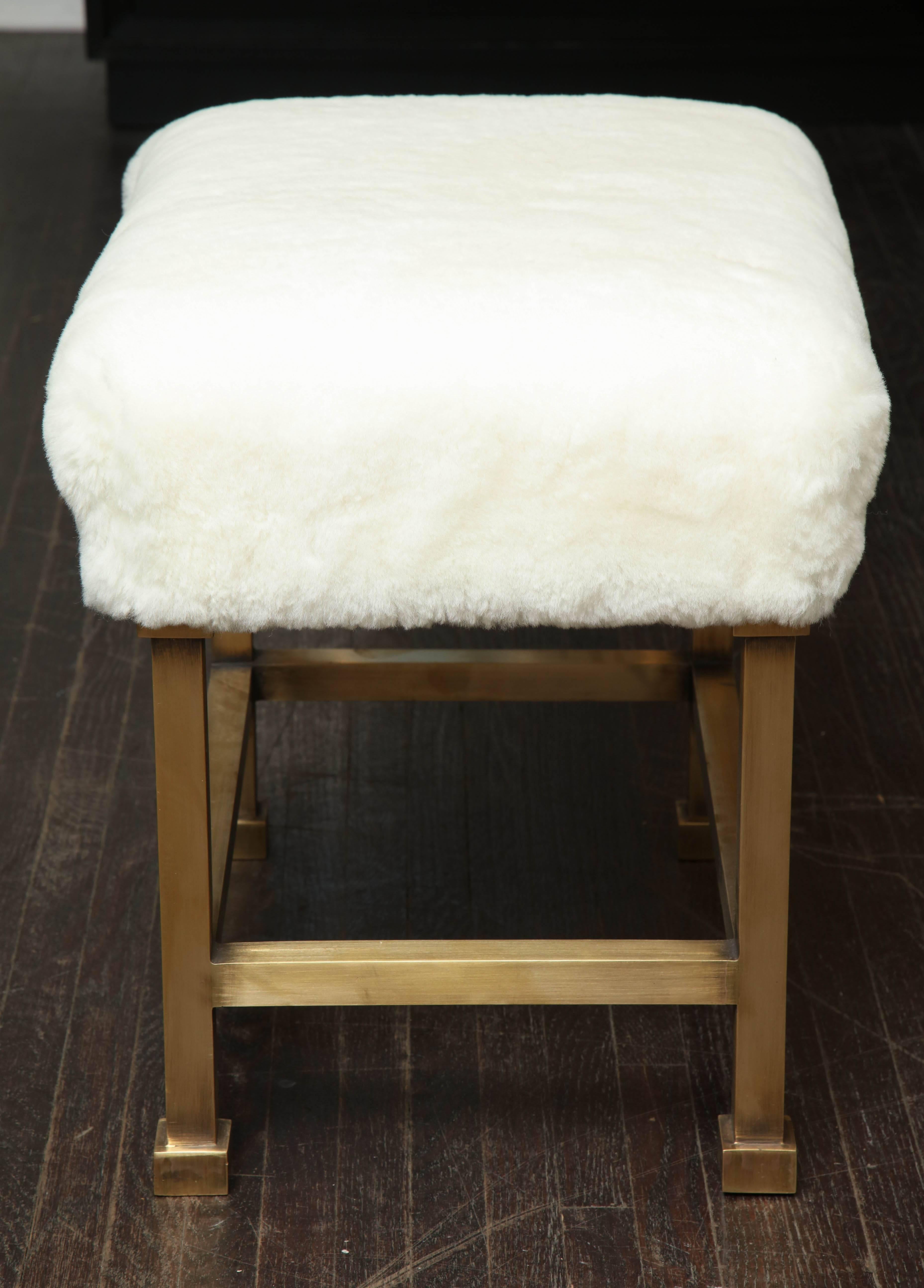 A chic pair of made-to-order stools with white shearling upholstery top and metal legs in light antiqued brass finish. The shearling used on the stools is genuine and may have subtle tone variations as natural product. A shearling sample for