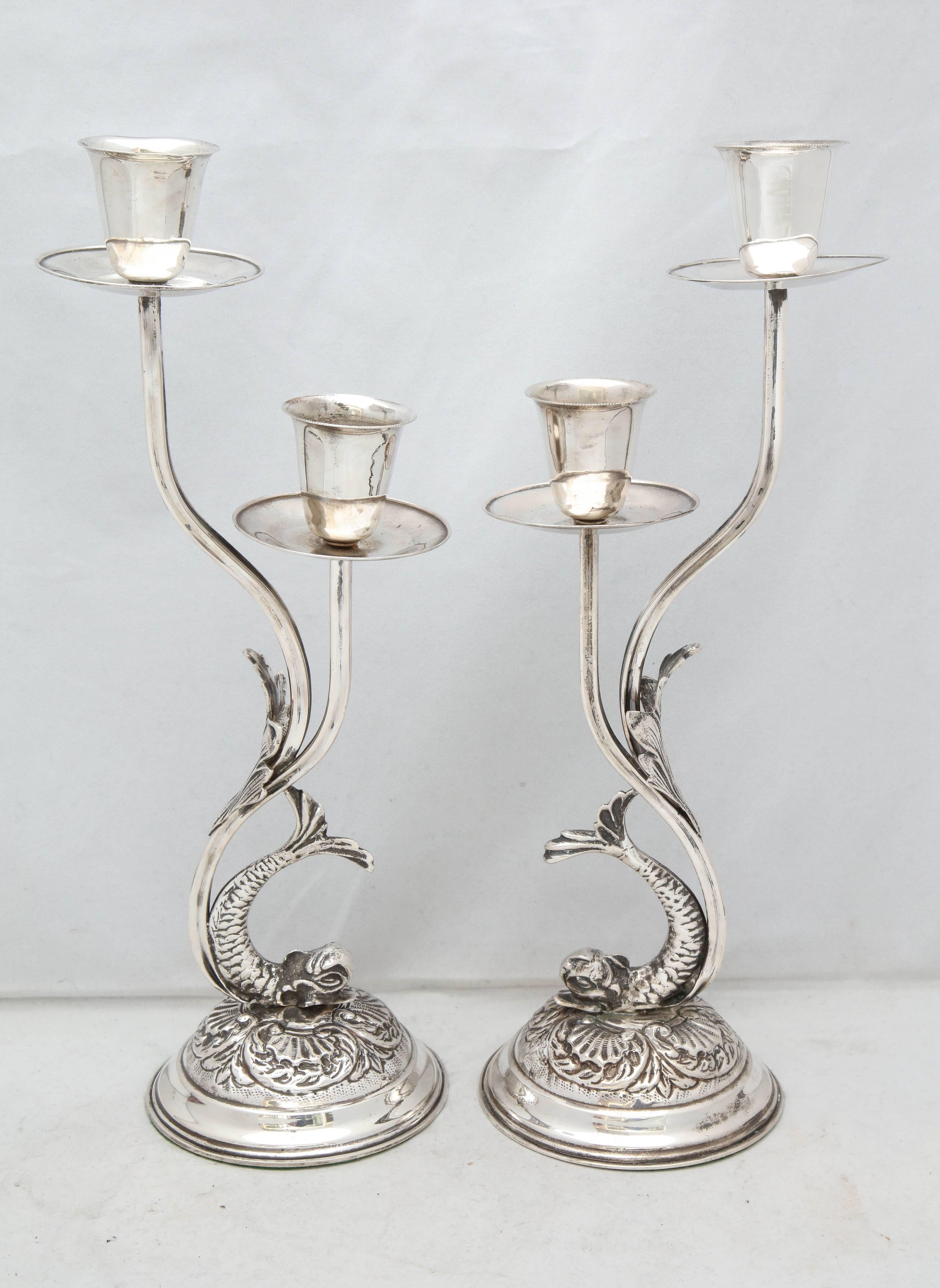 Unusual pair of Art Nouveau style Continental Silver (.800), Dolphin-form candlesticks, European, circa 1930s. Dolphins and sea flora form the column of each candlestick, which will take two candles. Each candle cup has a beaded rim and a pricket