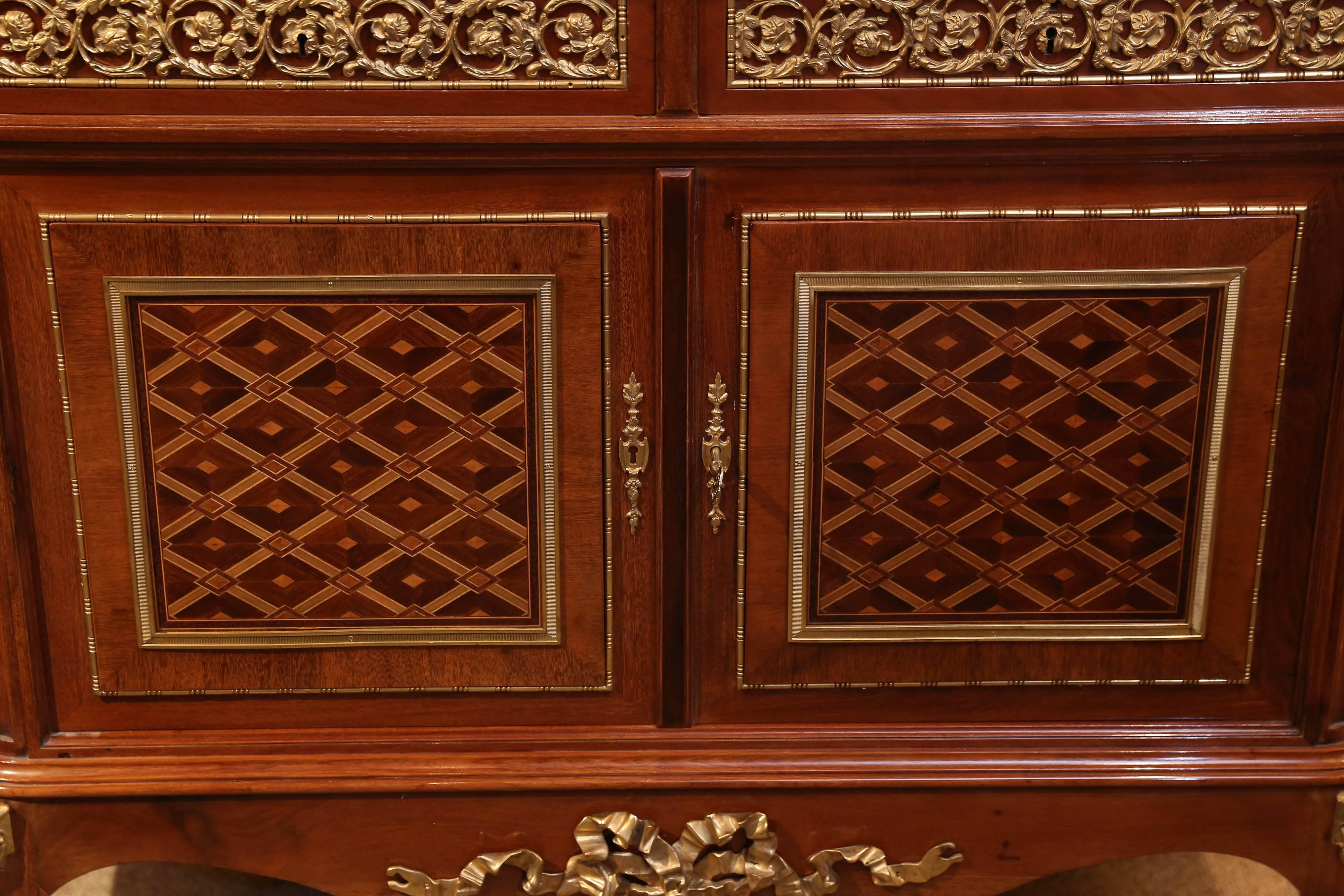 Early 20th century, the rounded rectangular breakfront; the top above two
Frieze drawers enclosing blossoming rose rinceaux pierced bronzes over paired doors inlaid with rosewood and satinwood lozenge patterned panels within Mille dais trim framed
