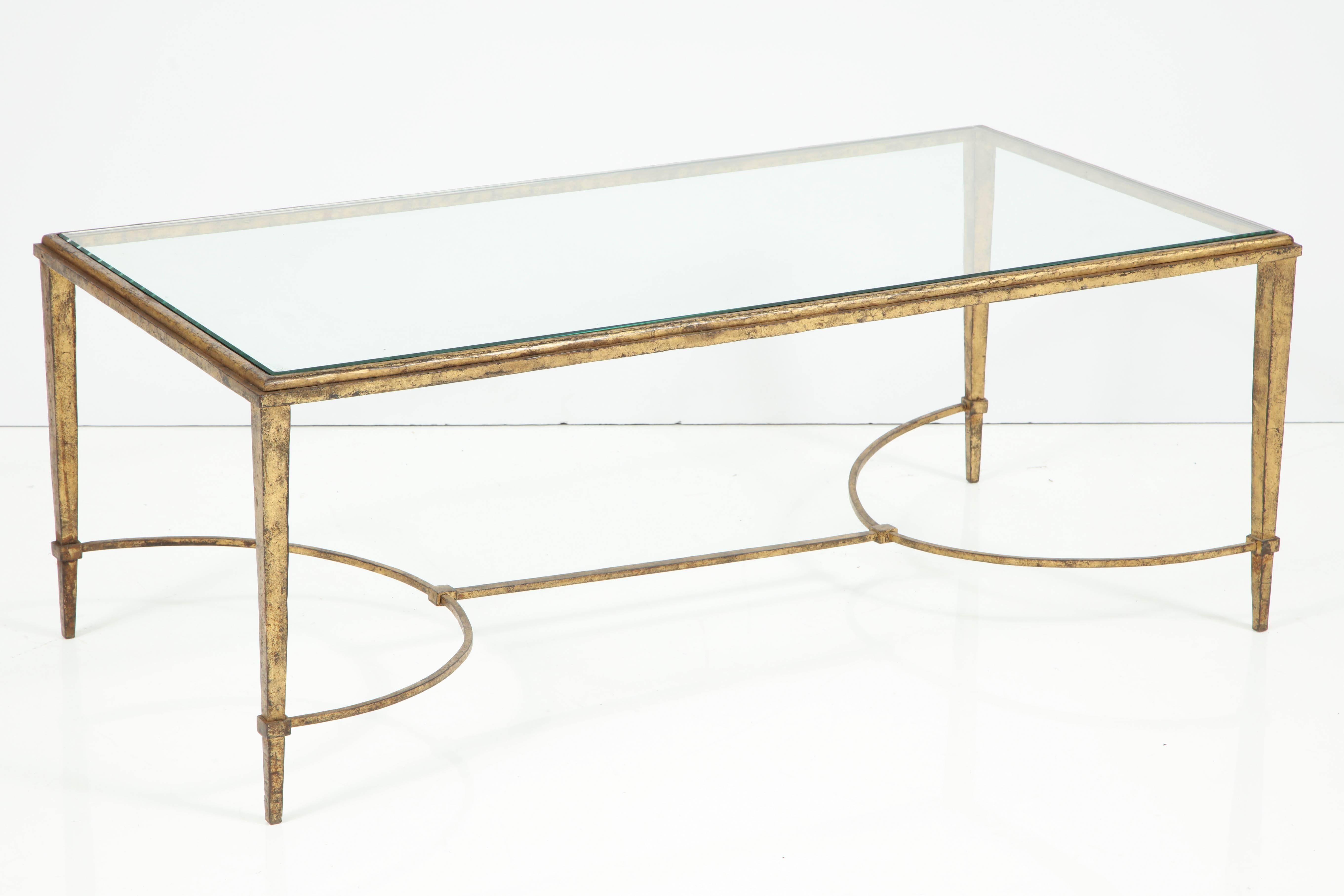 An understated, yet very chic and elegant cocktail table attributed to Maison Ramsay. The frame is gilt iron, with slightly tapered legs connected by a curved stretcher. The beveled glass sits atop a stepped frame. The clean lines of this piece
