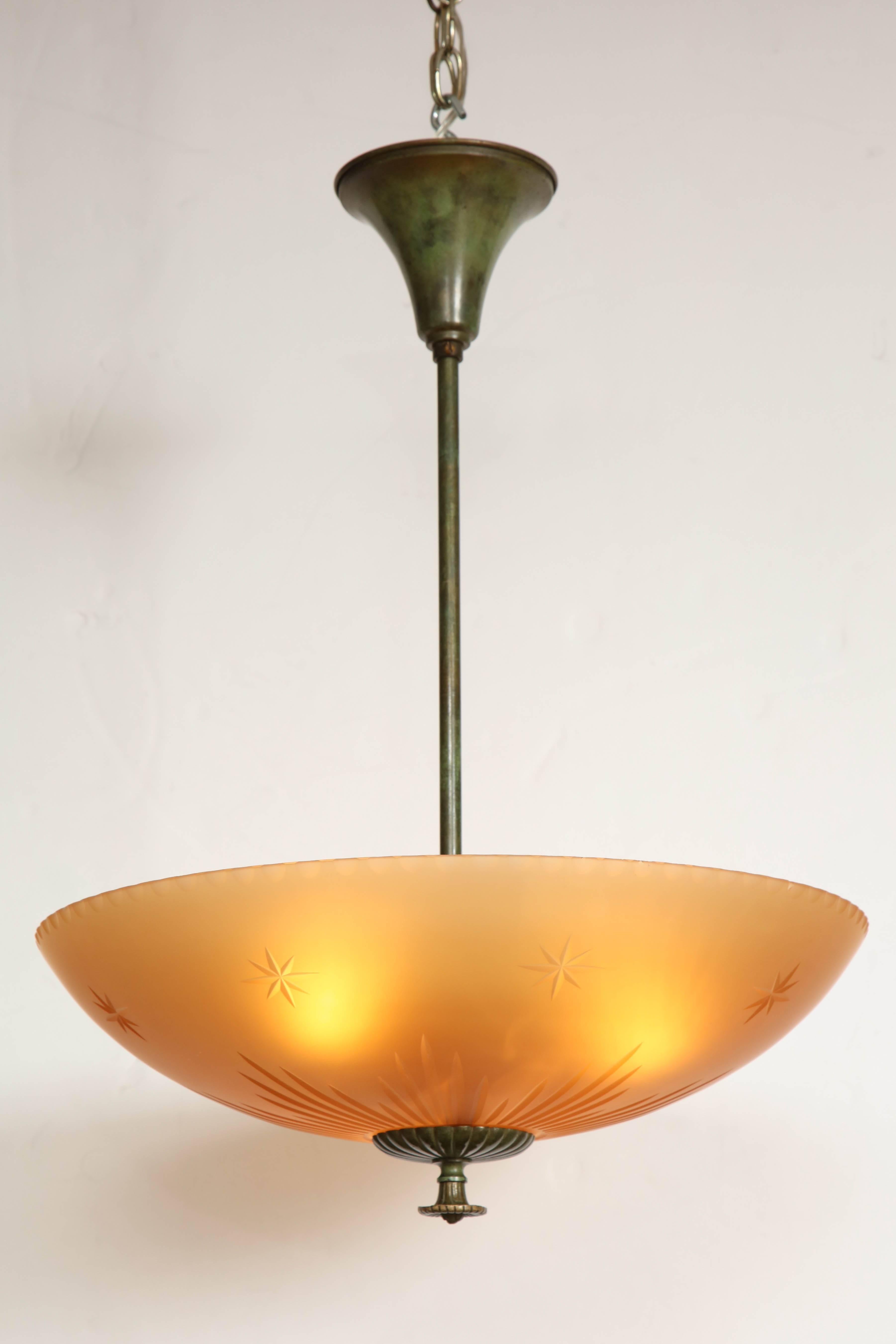 A Swedish patinated brass and amber cut-glass pendant, circa 1940s, with a plain rod stem supporting a glass bowl form shade with cut stars and channels, ending with a patinated brass gadrooned plate and finial. 

Rewired for the US 3 x 60watts