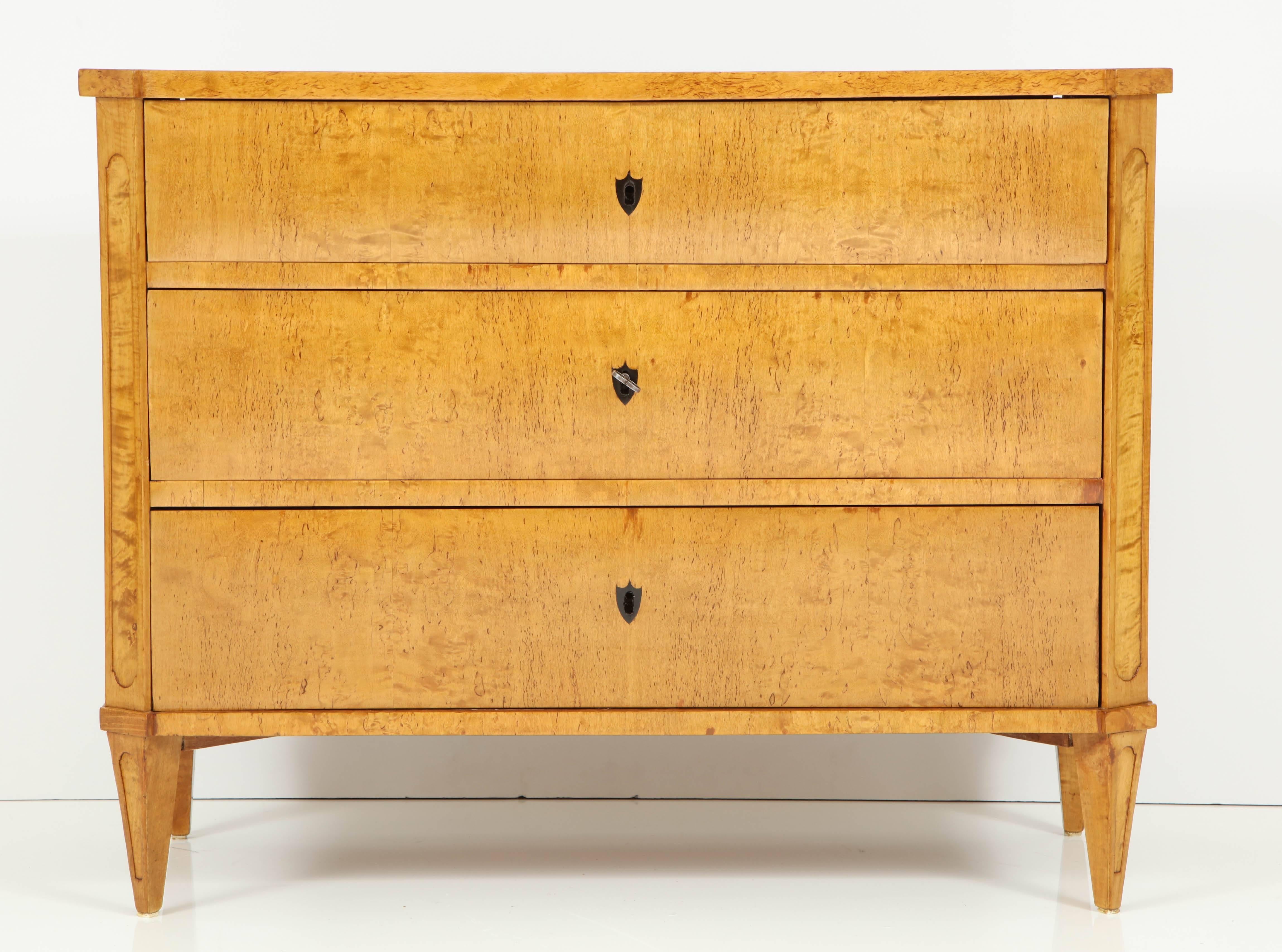 A Swedish late Gustavian/early Karl Johan, birch root commode, circa 1820s, the rectangular top with canted for-corners and conforming channeled sides, three long drawers, raised on square tapered and channeled legs.

