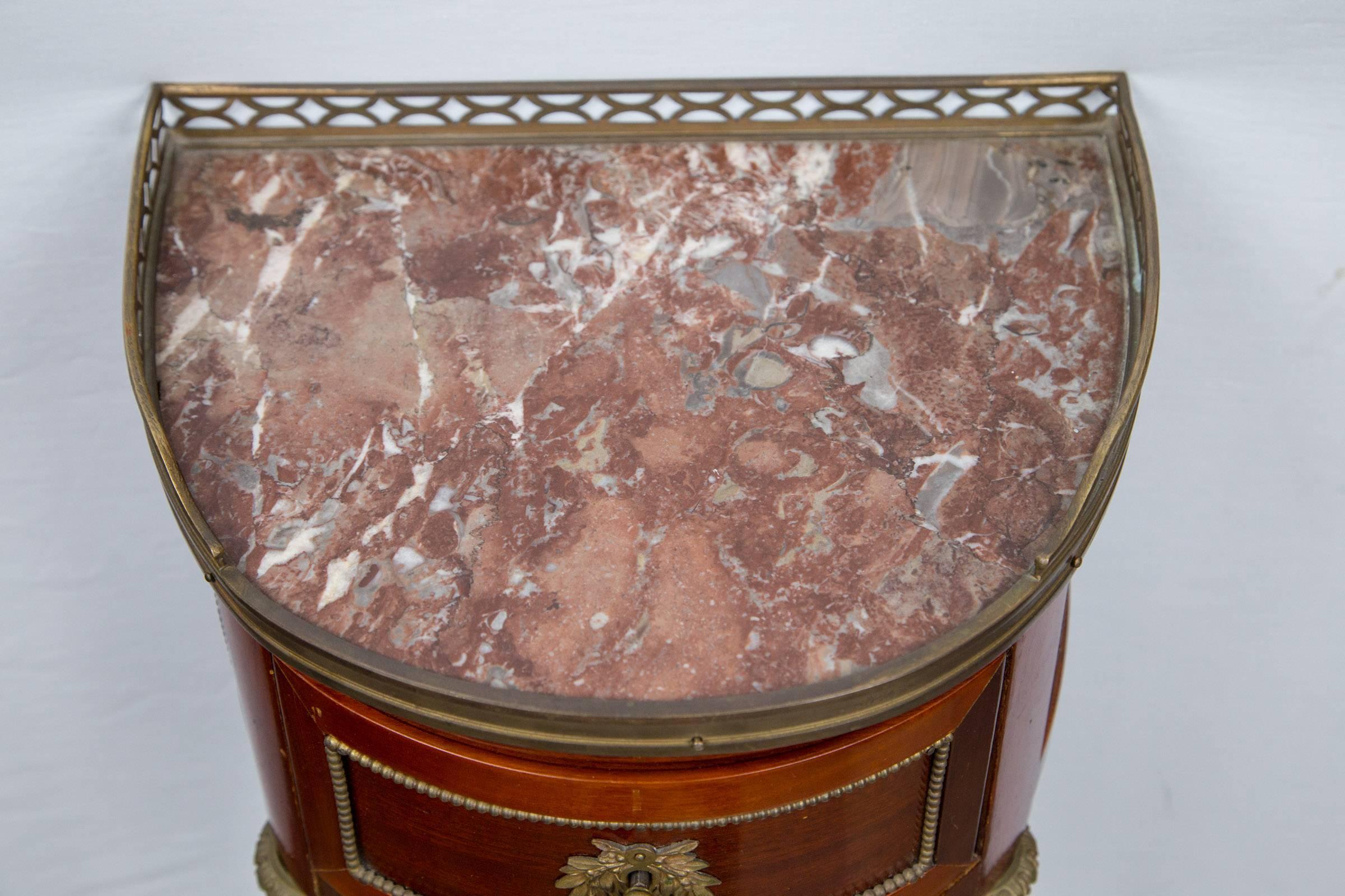 Dating from the end of the 18th century, these have liver, white and grey marble tops, surrounded on three sides by a brass gallery. Each has a single drawer with lock. Round tapered legs with stop flutting surmounted by a brass capital. The drawers