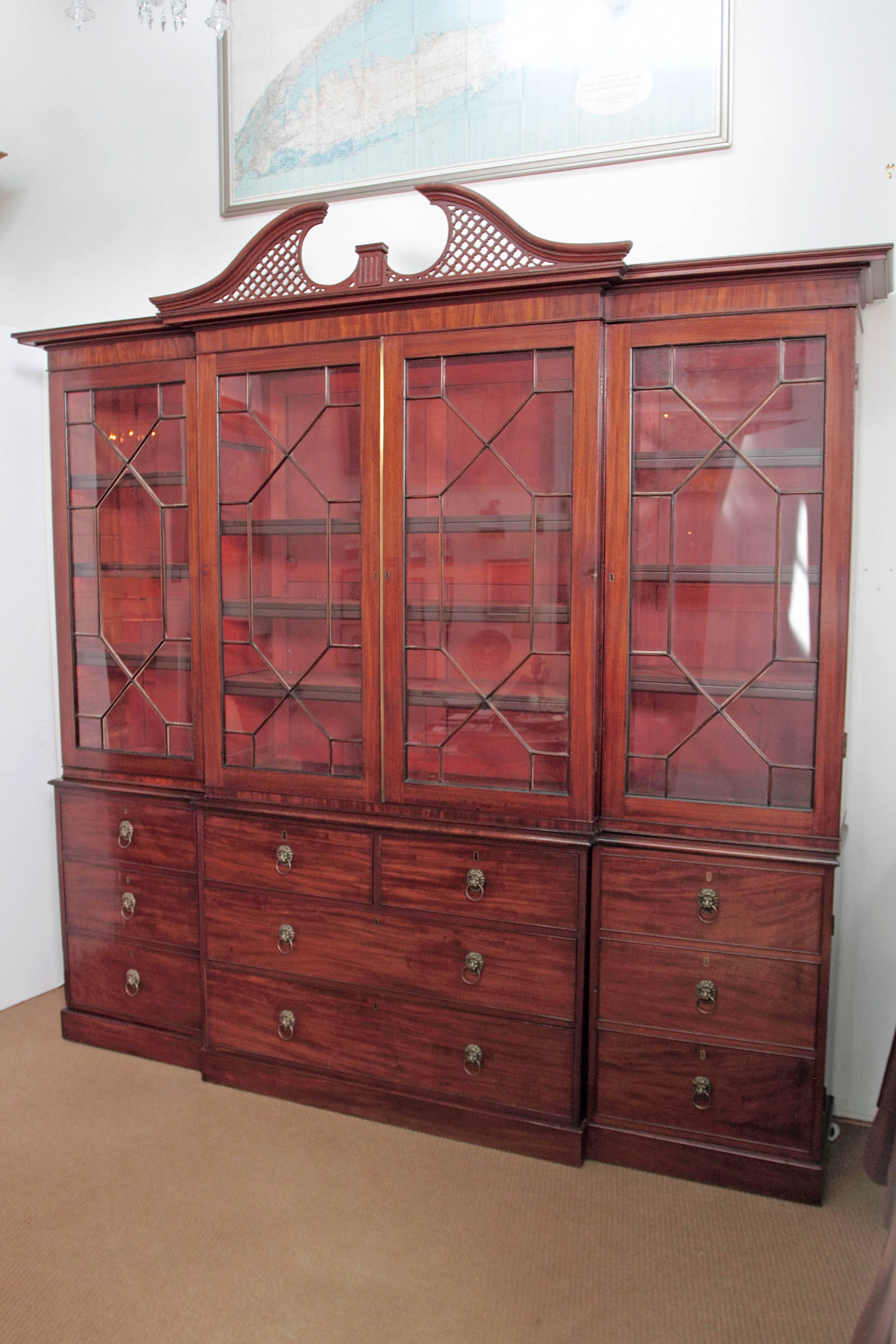 An elegant period George III mahogany breakfront bookcase / China cabinet with simple cornice and split pediment with lattice. Four (4) mullioned glass doors at the top with shelves inside. Bottom portion has two (2) small drawers above two (2)