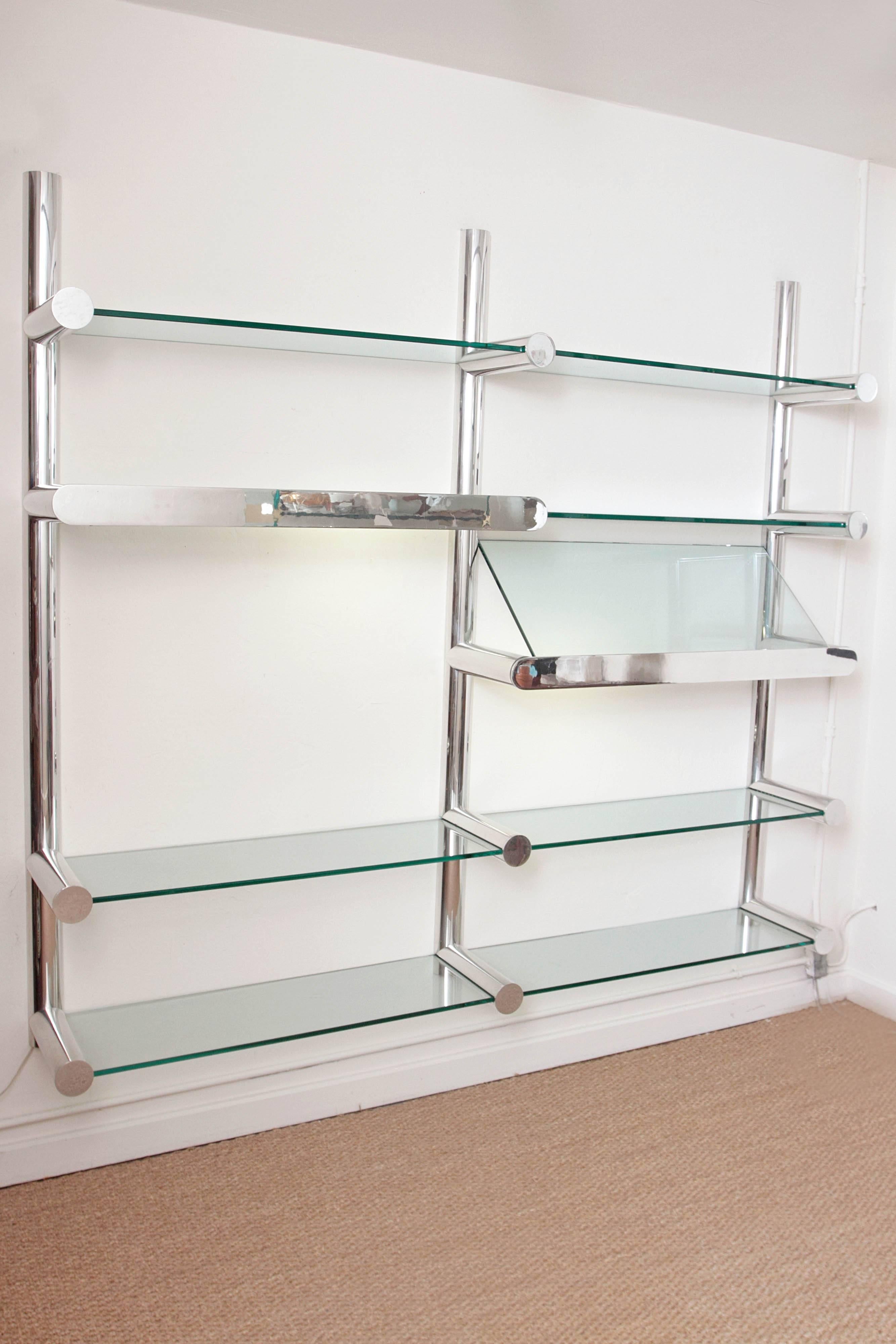 A wall-mounted polished aluminum and glass shelving unit with built in illumination. The polished plate front conceals two narrow florescent tubes which shine up and down.

They were manufactured in the 1970s in the USA.