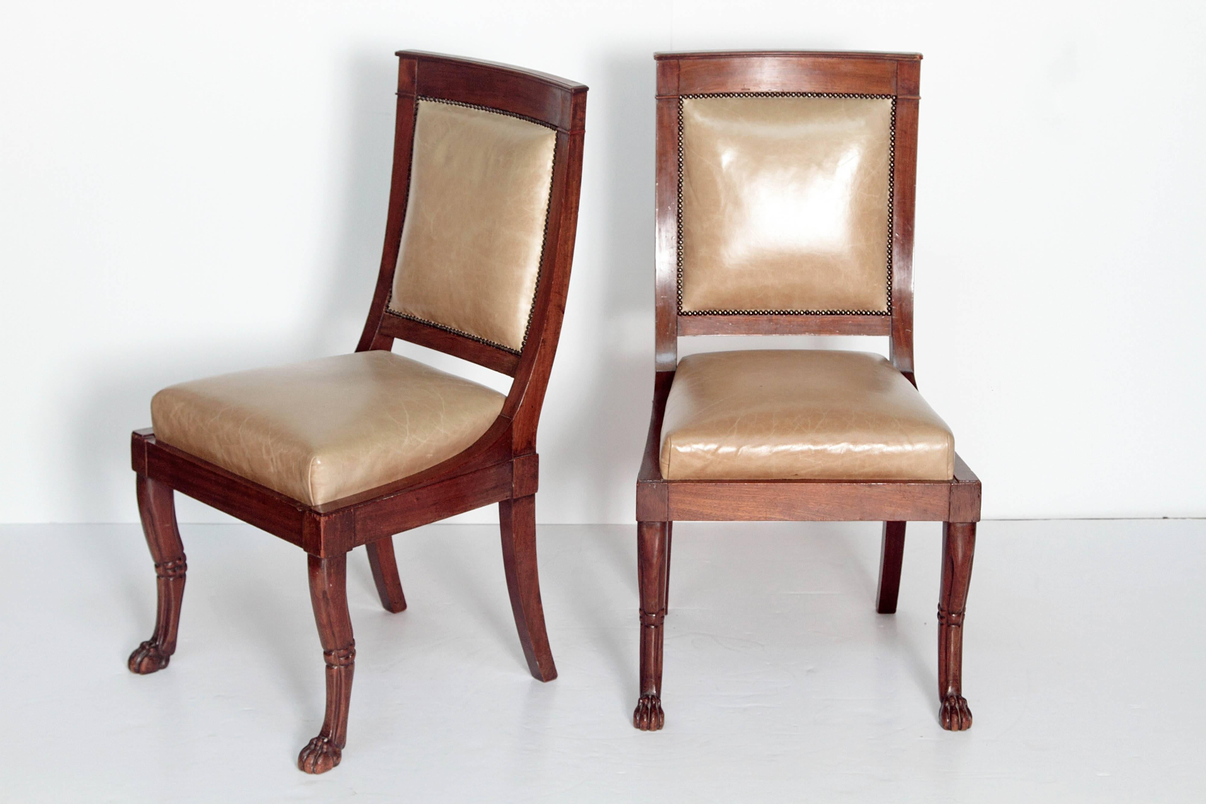 A pair of French neoclassic period chairs. Wood framed backs and seats with paw feets. The chairs are upholstered in beige leather.