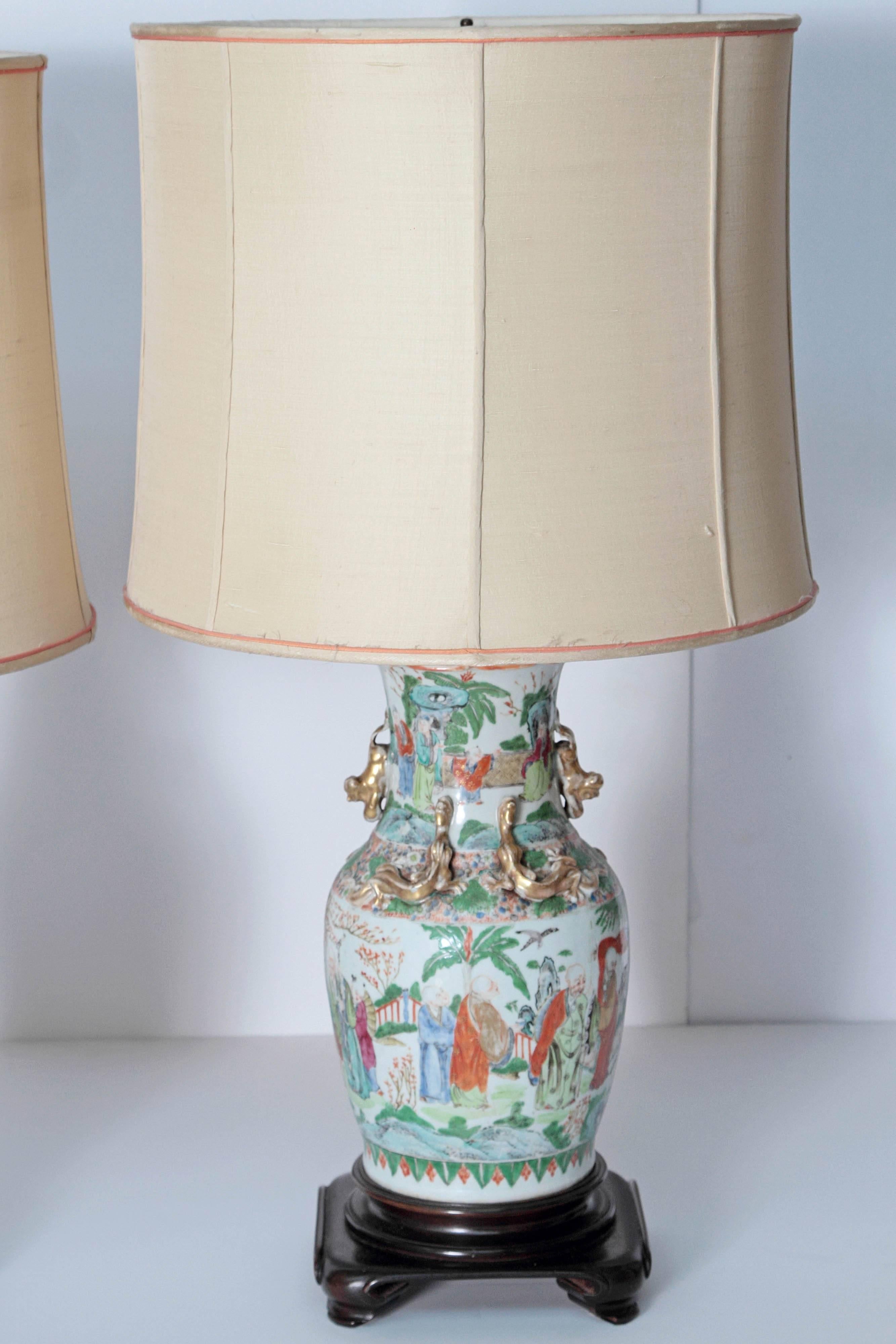 A pair of early 19th century Chinese porcelain vases mounted as lamps. White background with predominately orange and green wise men in landscape. Gilt dragon and foo dogs at shoulders.
Silk shade trimmed in rose. Vases mounted to wooden