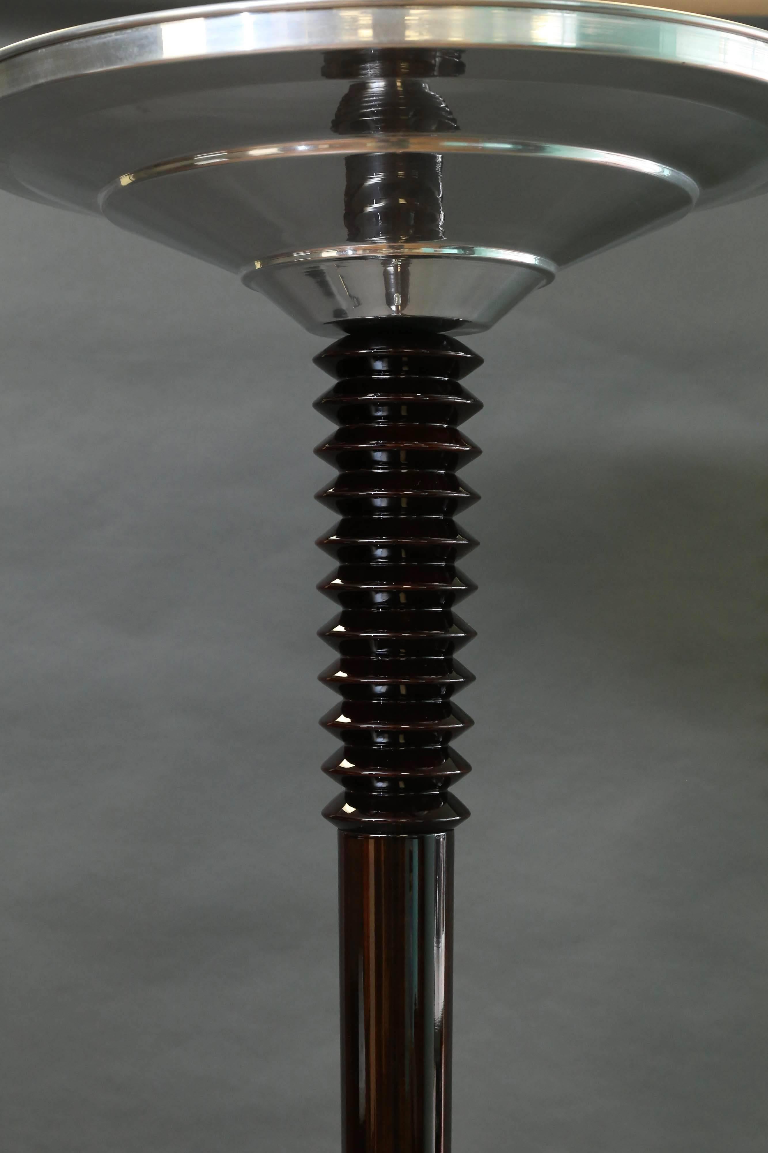 A bowl shape chrome lampshade is connected to the main pole and with the help of a chrome spike transfers to the wooden thick stabile base of the lamp. Due to the highly polished chrome of the lampshade, the light is strongly irradiates and spreads