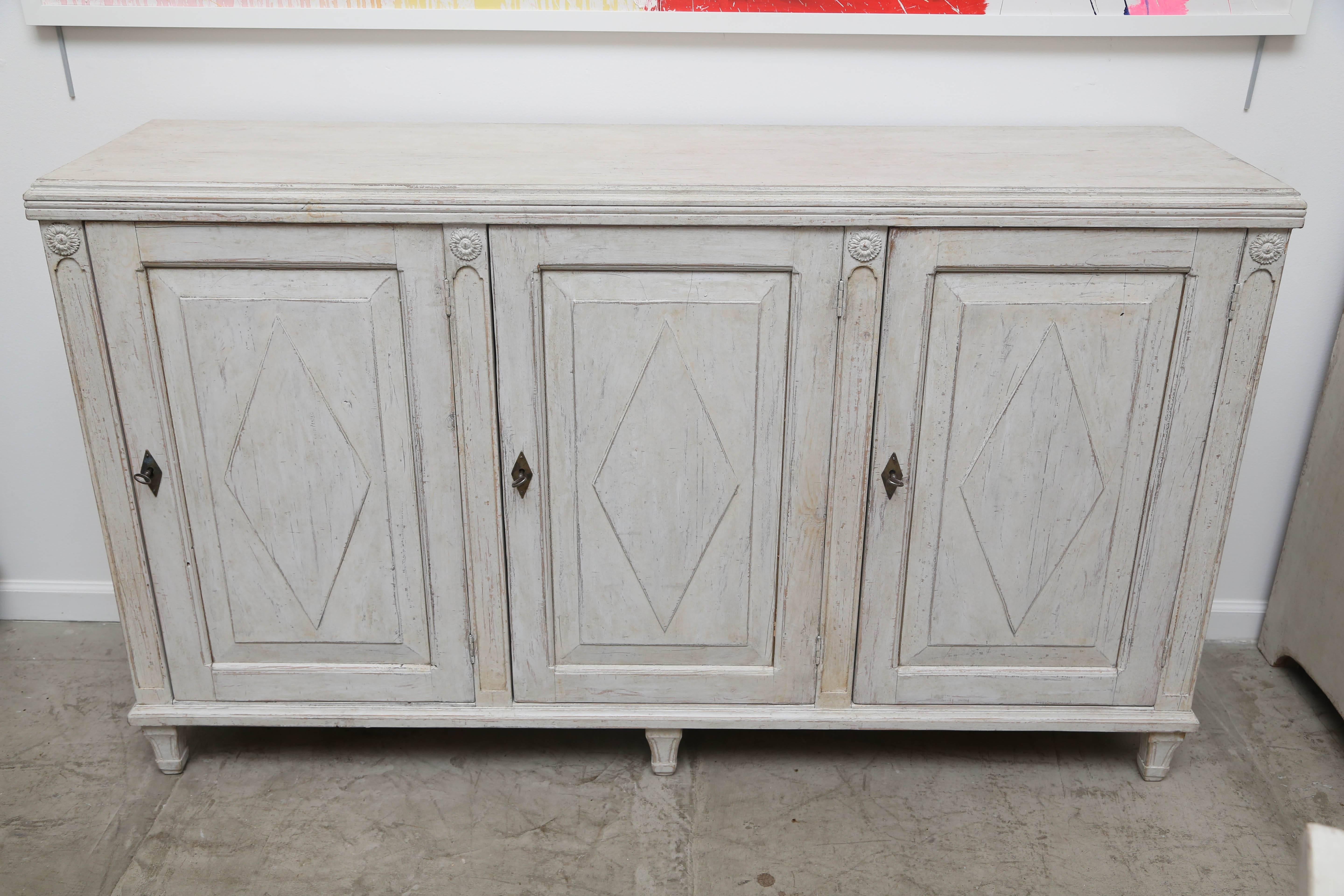 Antique Swedish Gustavian style painted three-door buffet, the doors have raised panels with a diamond motif in the centre of each, simple top with crown molding border. Carved arched design between each door and carved rosette
at top of each arch.