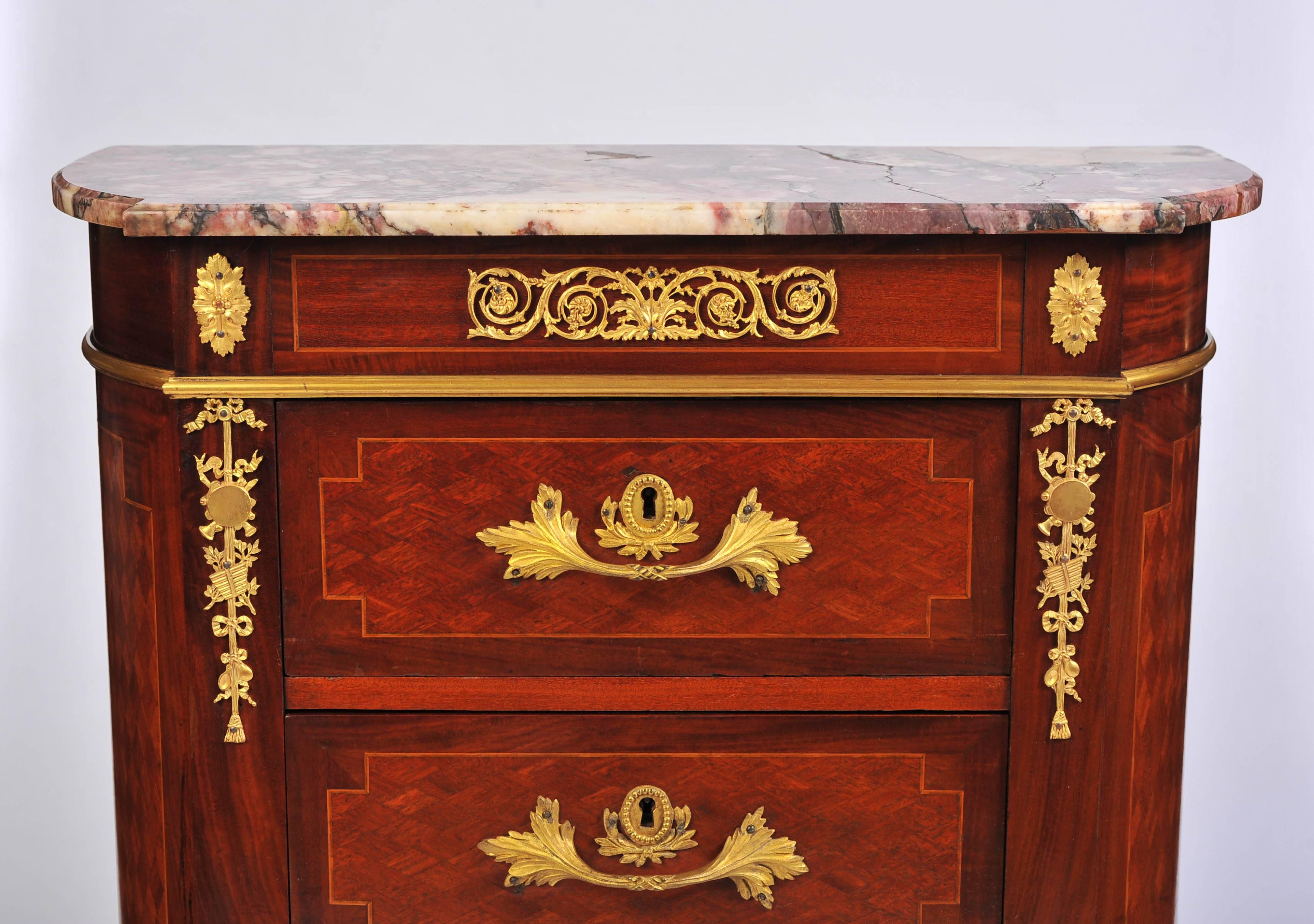 A charming Fin de Siecle mahogany petite commode in the Louis XVI style, the three drawers each with double throw locks below the original variegated marble top and enriched throughout with fine quality gilt metal mounts.
   