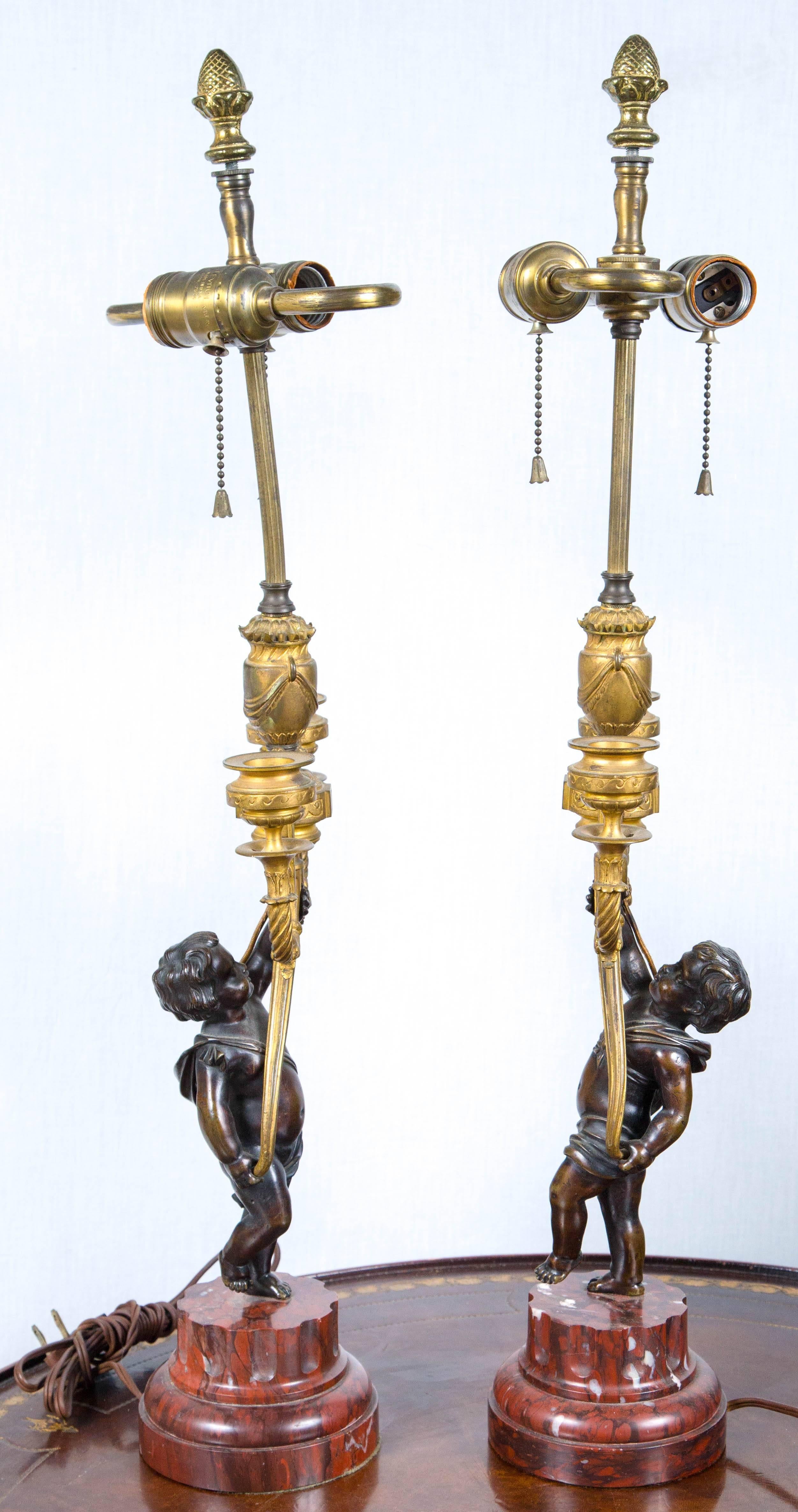 Each putto holds aloft a pair of gilt bronze candle cups. Currently wired as table lamps.
They stand upon stepped and fluted rouge royal marble bases.
S cluster bulb lamping.
overall height 26 inches to the top of the finial
16 tall to the top