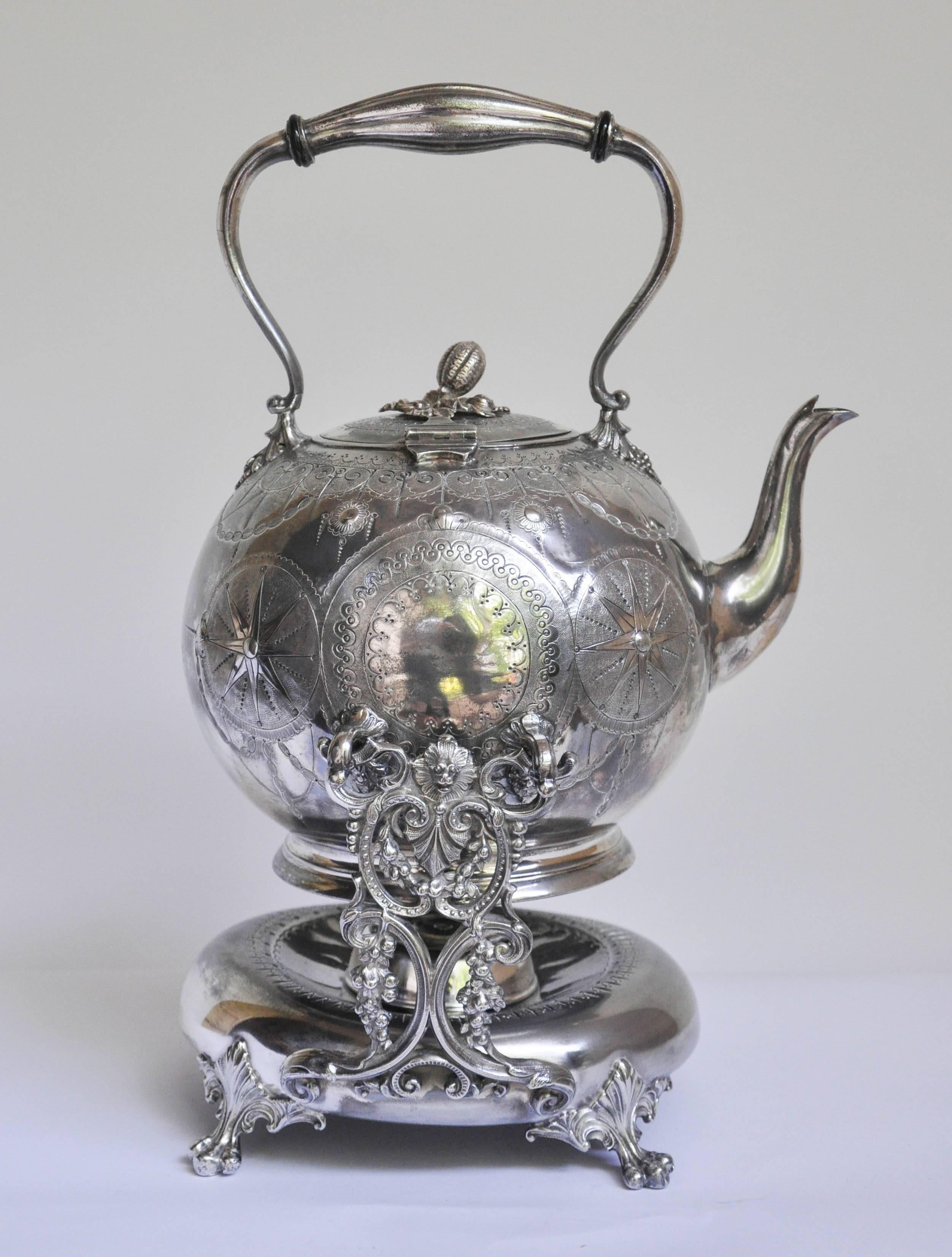 Charming English Regency style tilting tea kettle on a lamp stand. The kettle is delicately chased with a swag-like design, lovely repoussé work decorates the center of the barrel in the form of sunbursts and crests. The hinged lid has a finial
