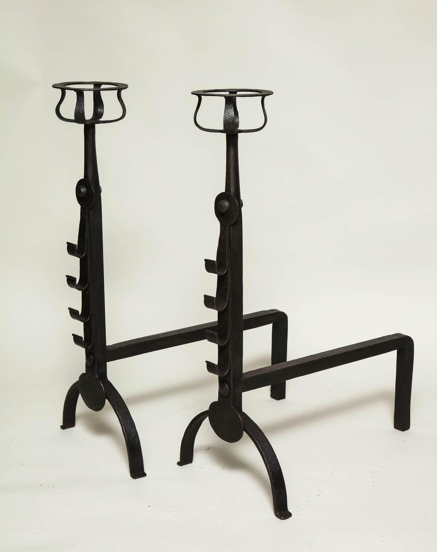 Fine pair of English wrought iron Cotswold school andirons in the manner of Ernest Gimson, having basket tops over hand-hammered shafts with flattened penny applied spit supports, standing on simple arched legs. 

Ernest Gimson, Ernest and Sidney