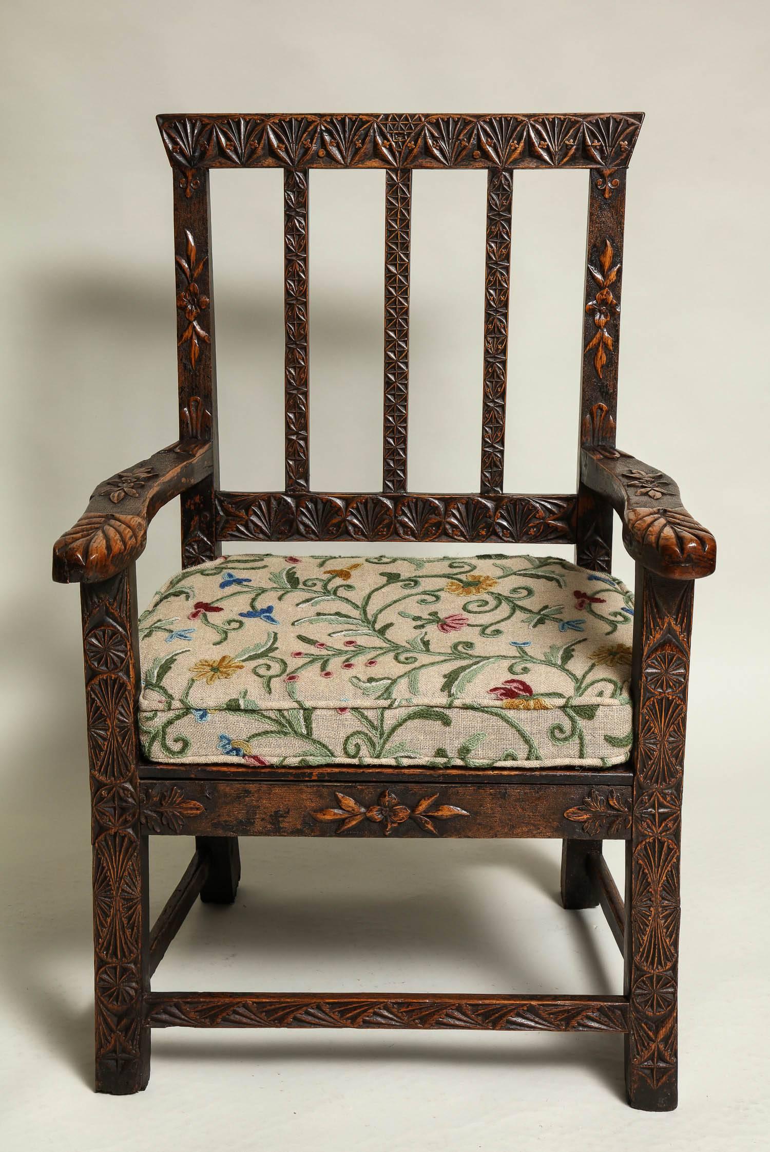 Most unusual English oak armchair with profuse carving to rails, crest and arms and possessing great color and patination. Custom crewelwork cushion over later plank seat, carved to simulate rest of chair.
