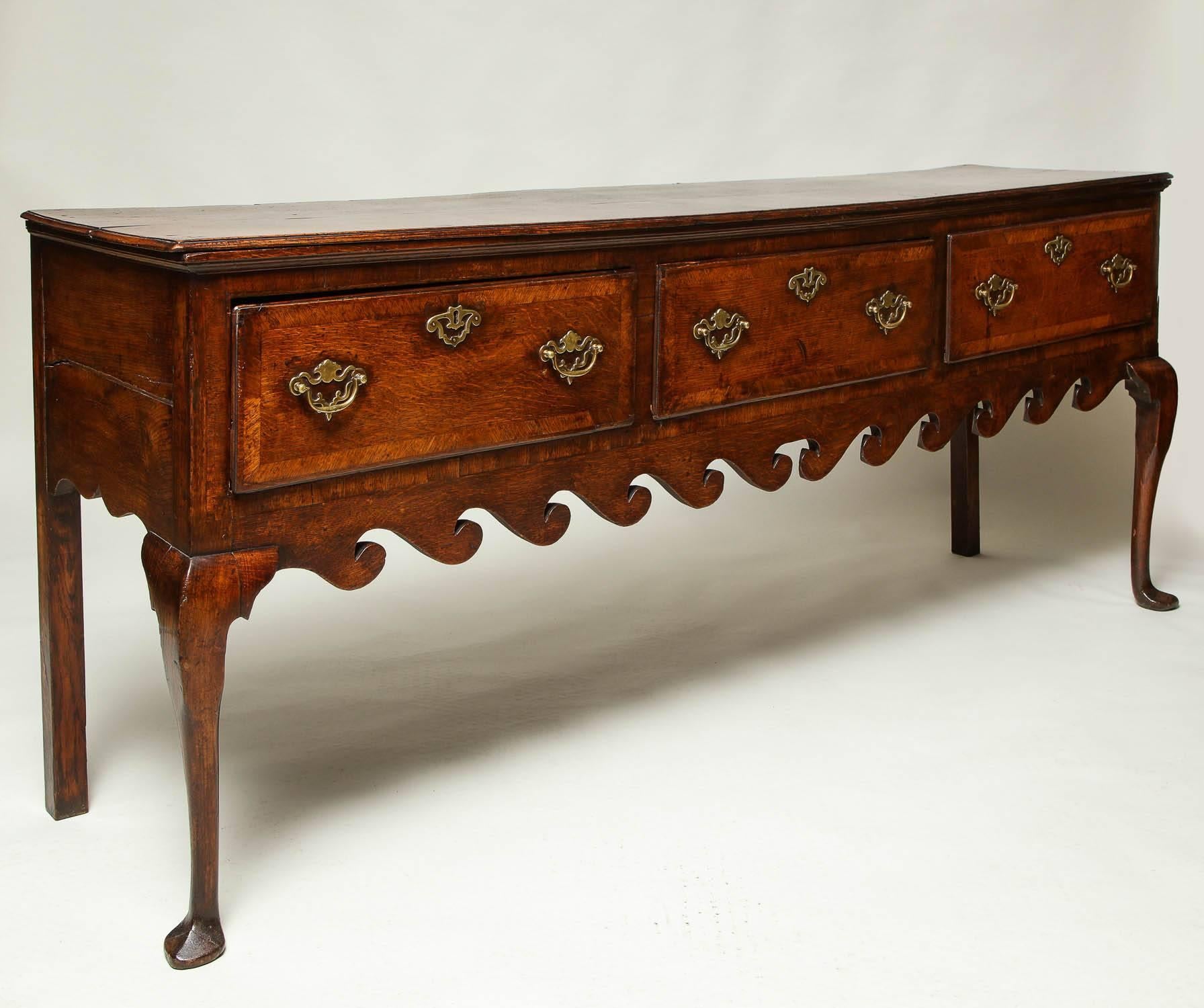 A fine George III English oak low dresser or server with three mahogany cross banded drawers standing on cabriole front legs with slipper feet, over richly scalloped "wave" apron, the whole possessing great rich color and patination.