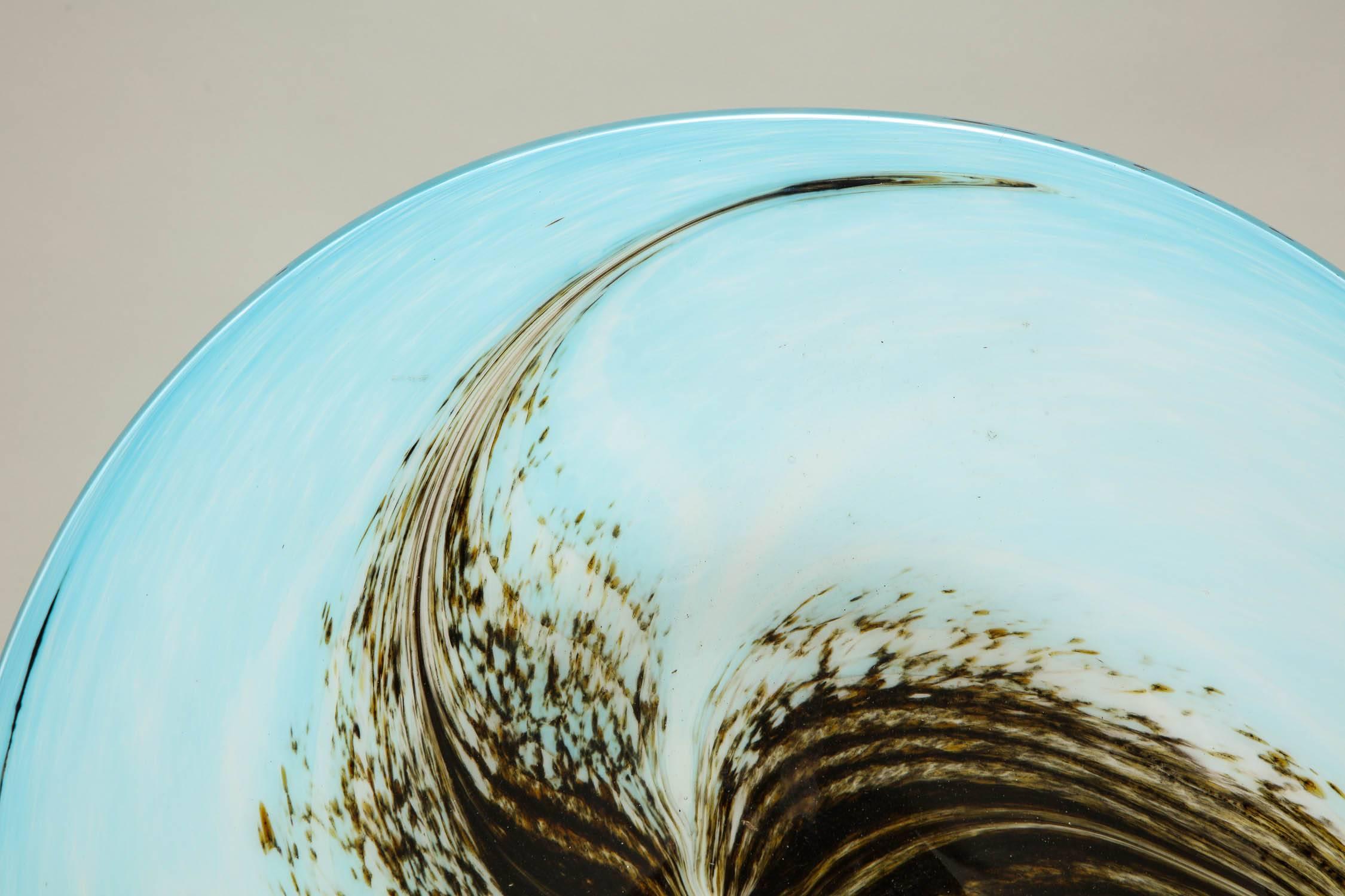 An English 1950s art glass dish form charger having a turquoise rim, swirling into a milky blue, and a central image of three spinning chocolate seed pods.